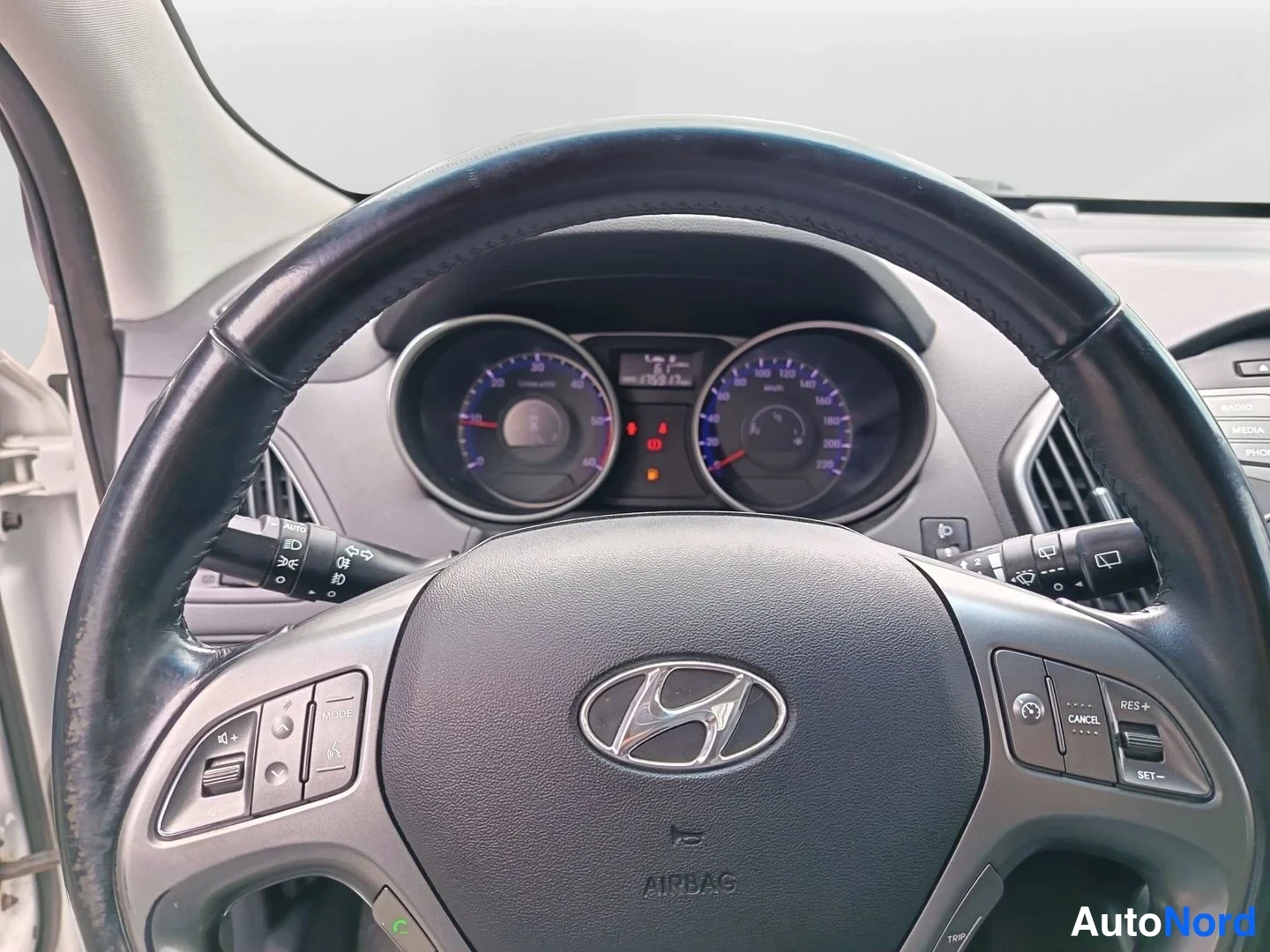Muu: Ohjauspyörän lähikuva: Hyundai-merkki, AIRBAG-teksti, monitoiminapit ja mittarit taustalla.