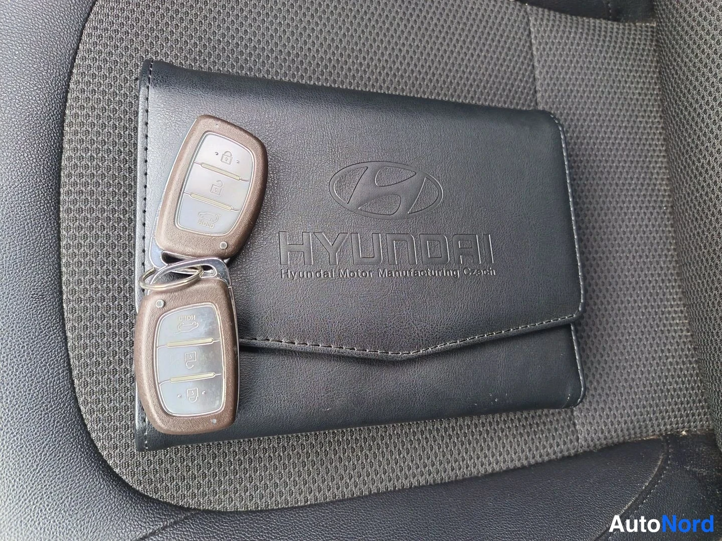 Muu: Kaksi Hyundai-kauko-ohjainta ja Hyundai-kansio istuimen päällä.