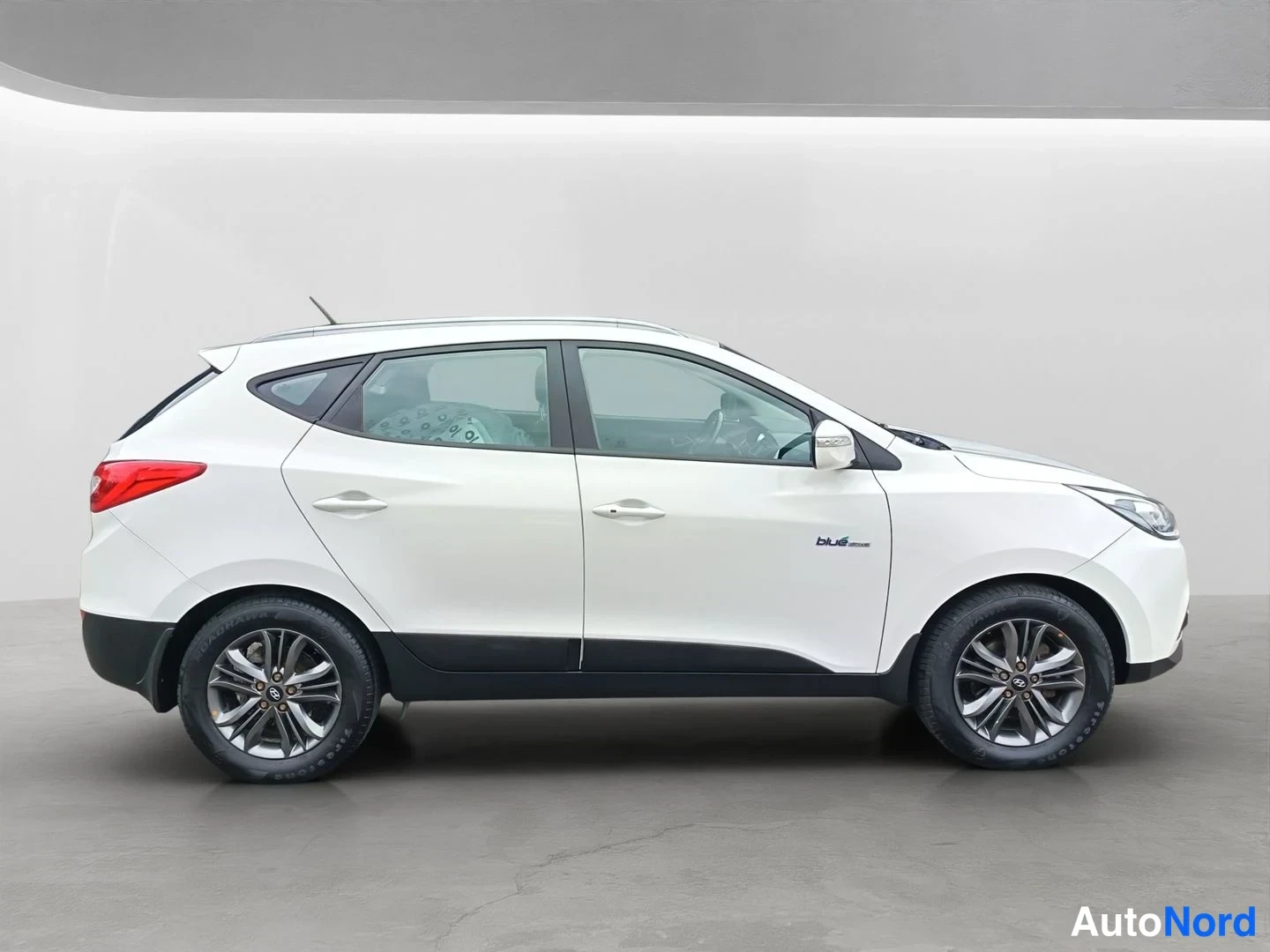 Sivulta: Hyundai ix35, sivukulmakuva, valkoinen koripaneeli, tummat alareunan listat ja tummat kevytmetallivanteet, pieni teksti 'blue' oven alla.