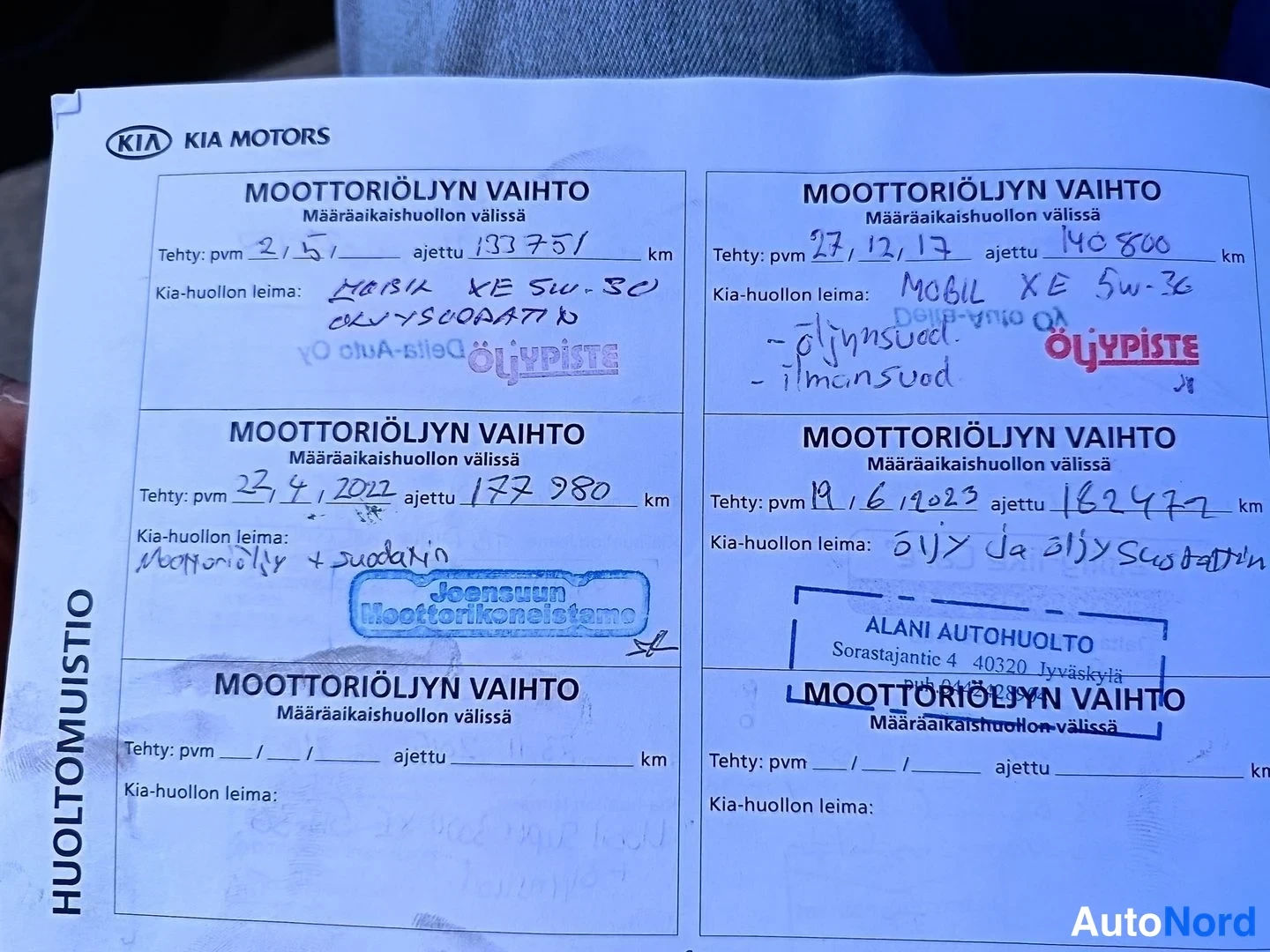 Muu: Kia-huoltokirjan huoltomuistiosivu, jossa moottoriöljynvaihto-merkinnät vuosilta 2015–2023 ja ajetut kilometrit 133751–182477, leimoina Öljypiste, Joensuun Moot