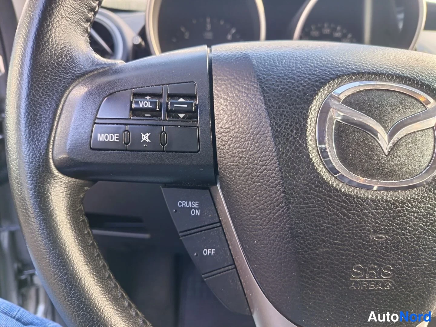 Yksityiskohta: Detailed shot of the left side of the steering wheel controls. Visible buttons include volume up/down ('+VOL', '-'), mode selection ('MODE'), a mute icon, and c