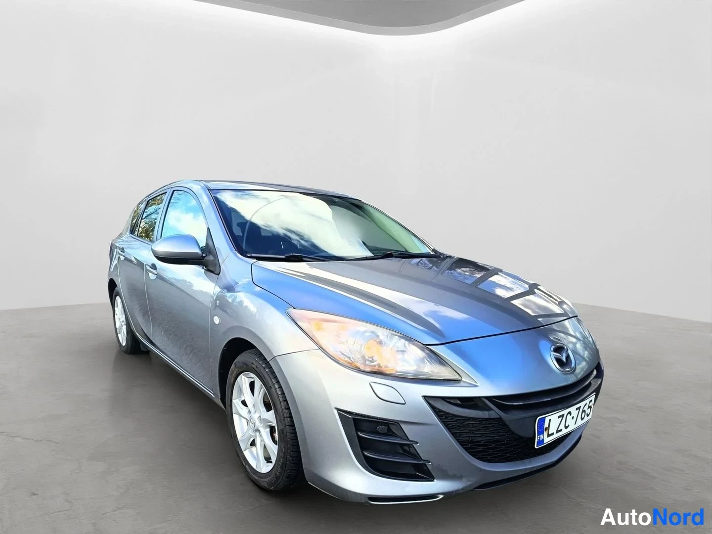 Etuviisto, nokka oikealle: Hopeanharmaa Mazda 3 -henkilöauto kuvattuna etukulmasta oikealta, rekisterikilpi.