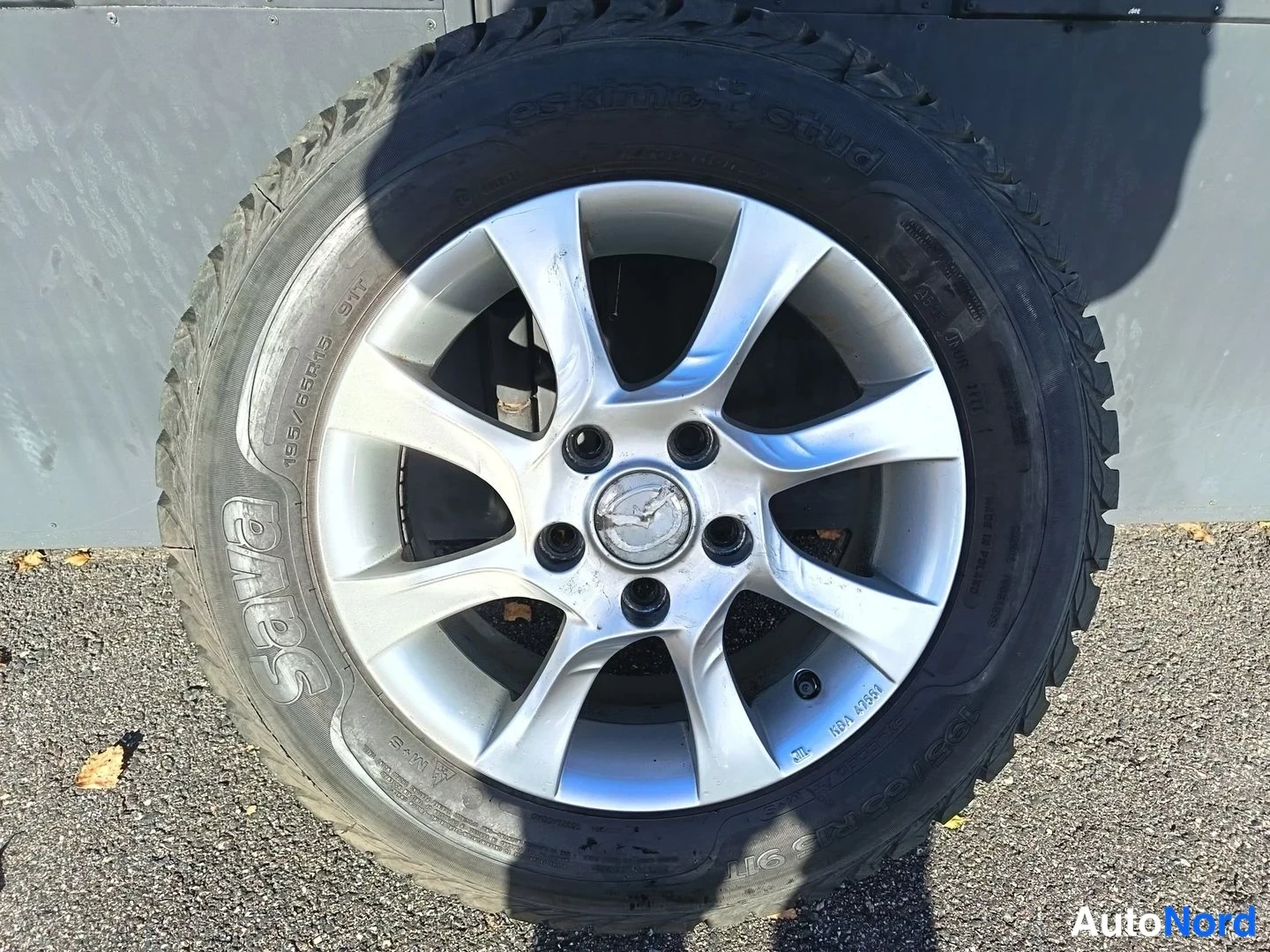 Yksityiskohta: Mazda-merkkinen hopeavärinen vanneren varapyörä tai irrotettu rengas, Sava-jokitankuu sivitysmalli, konepellin alla, kallistuskulmassa 0.7