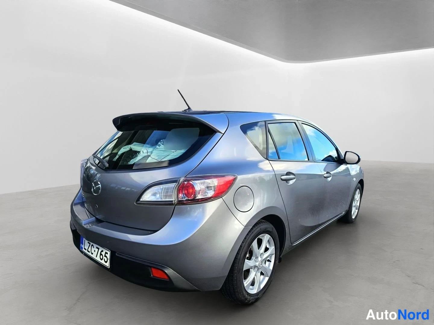 Takaviisto: Mazda 3 -viistotakakulma: auton takaosa ja oikea kylki harmaassa studiossa, rekisteritunnus.