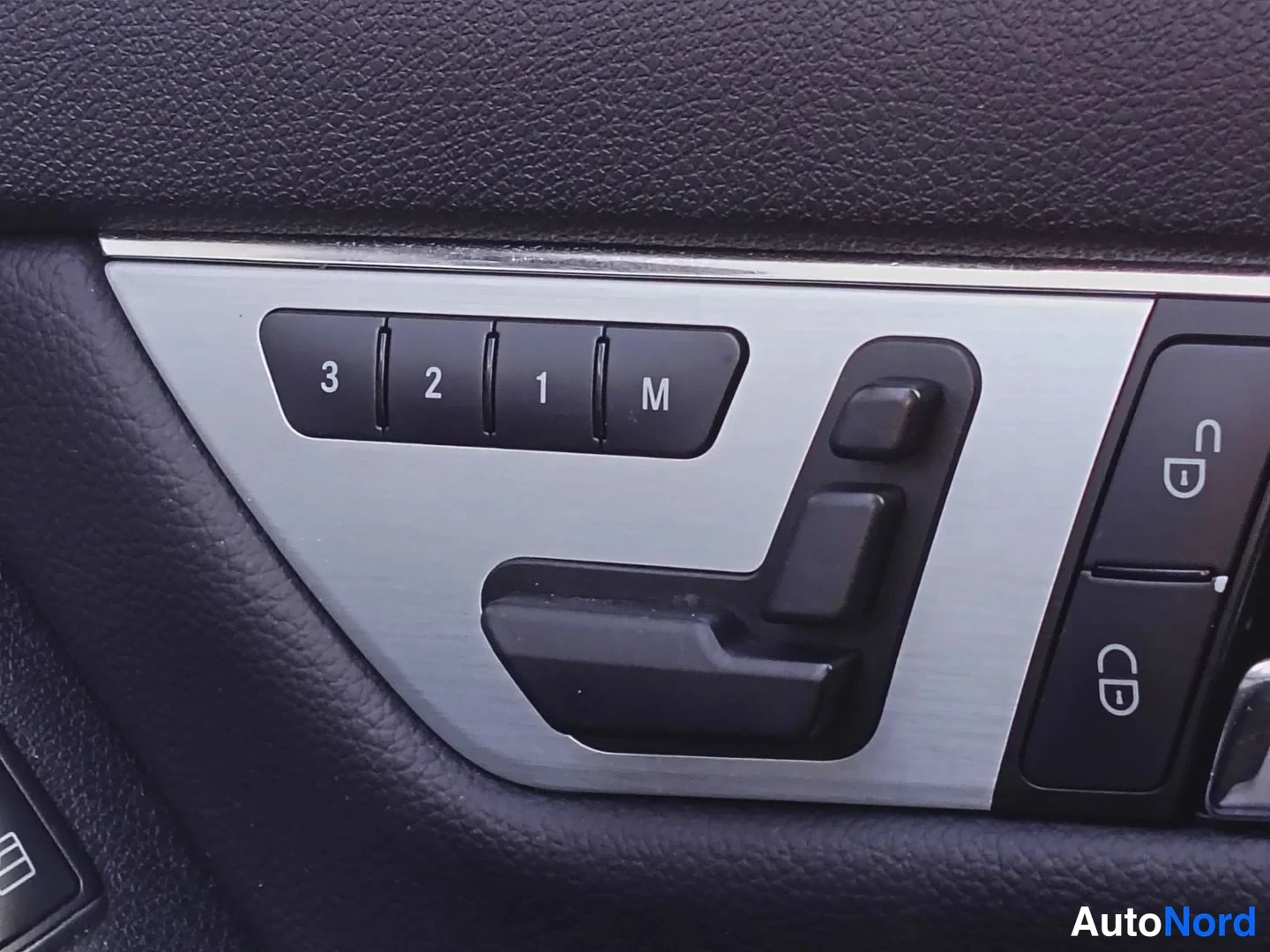 Yksityiskohta: Toisen oven sisäpaneelin metallikoriste: muistipainikkeet 3, 2, 1 ja M, sähköistuimen säätökytkimet sekä lukitus- ja avauspainikkeet.