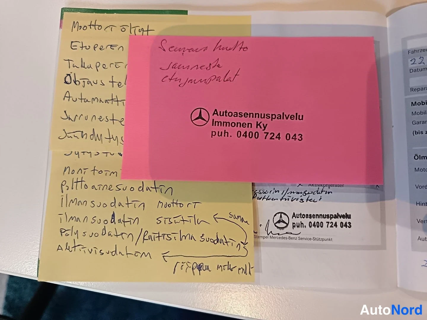 Yksityiskohta: Serviceheft-aukeama, jossa keltainen käsinkirjoitettu muistilista ja vaaleanpunainen kortti Autoasennuspalvelu Immonen Ky -yhteystiedoilla puh. 0400 724 043.