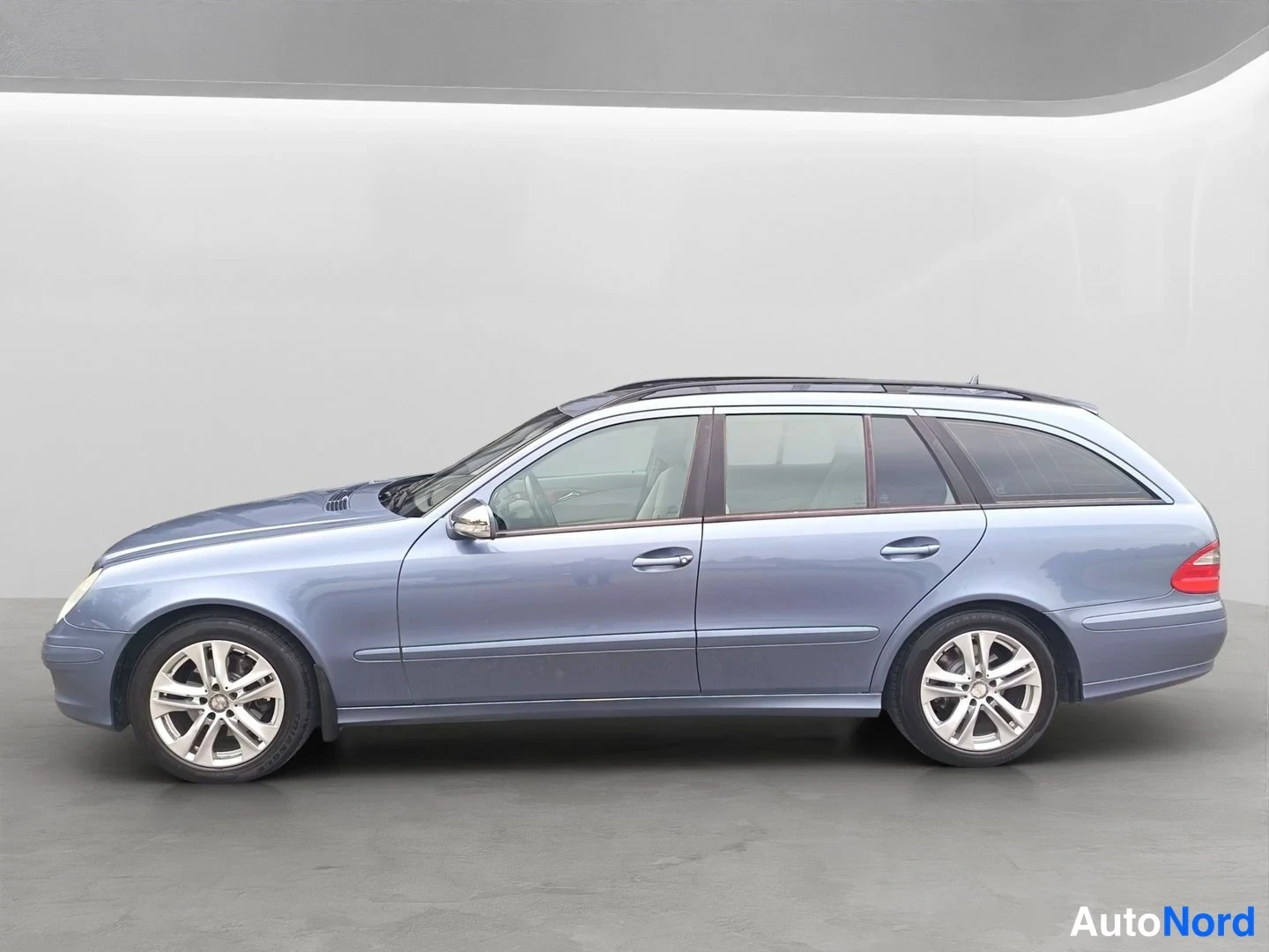 Sivulta: Sininen Mercedes-Benz E 320 CDI -farmari sivulta, auton oikea kylki ja kattokaiteet näkyvät