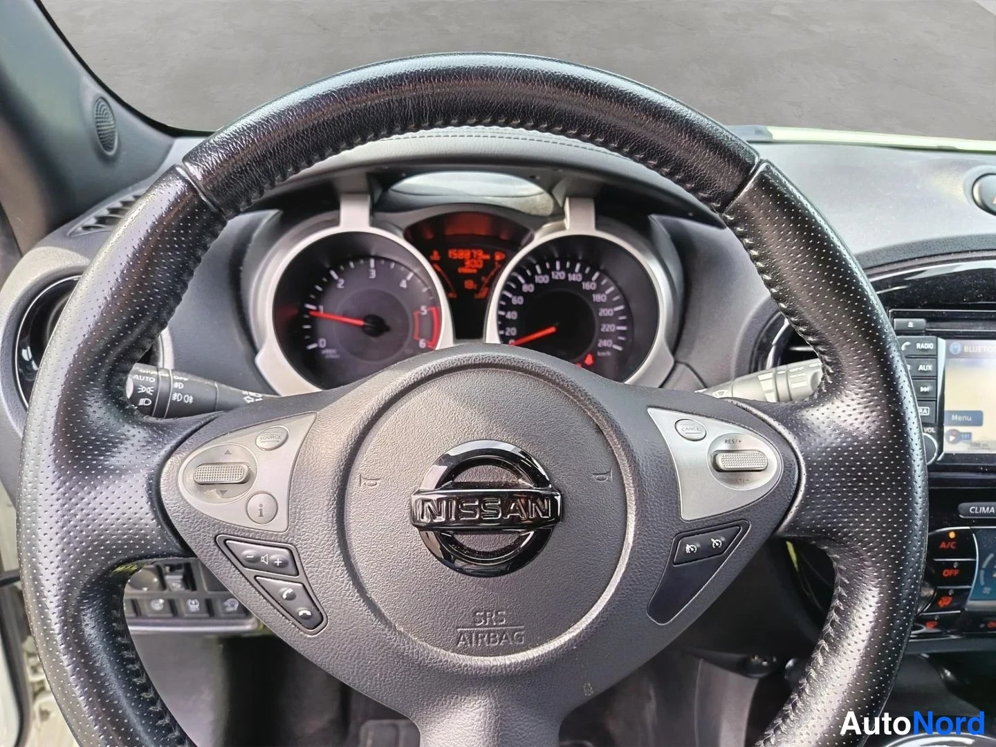 Yksityiskohta: Nissan-ohjauspyörän lähikuva, jossa multitoiminnot näkyvät vasemmalla ja oikealla, ilmatyynyteksti SRS Airbag keskirimmassa.