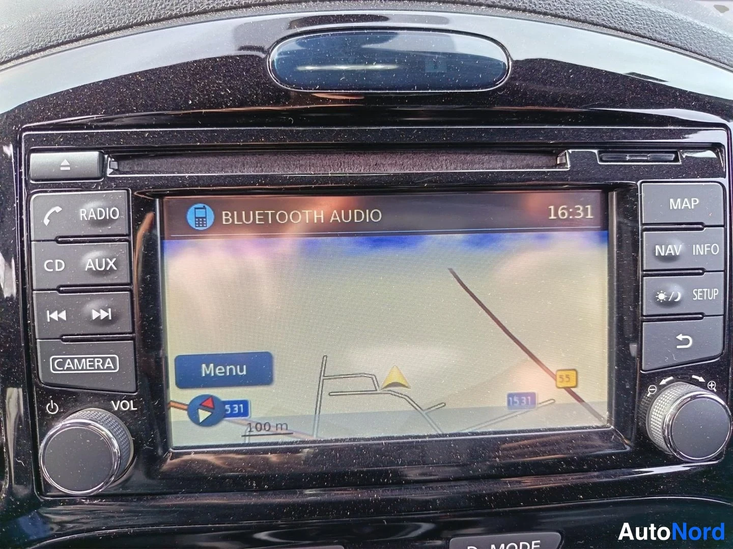 Yksityiskohta: Auton infotainment-näyttö näyttää karttaa ja tekstiä BLUETOOTH AUDIO, kello 16:31. Näytön ympärillä RADIO-, CD-, AUX-, CAMERA-, MAP- ja NAV-painikkeet.