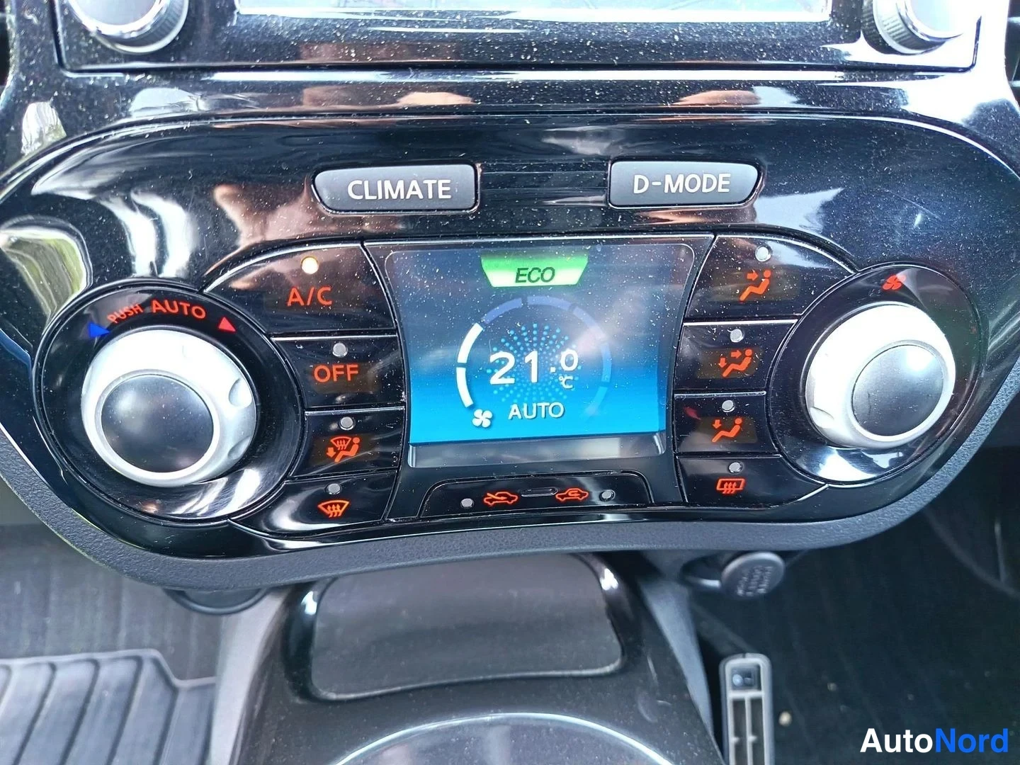 Yksityiskohta: Auton kojelaudan ilmastointipaneeli näytöllä, jossa lukee 21 astetta ja AUTO, sekä CLIMATE- ja D-MODE-painikkeet.