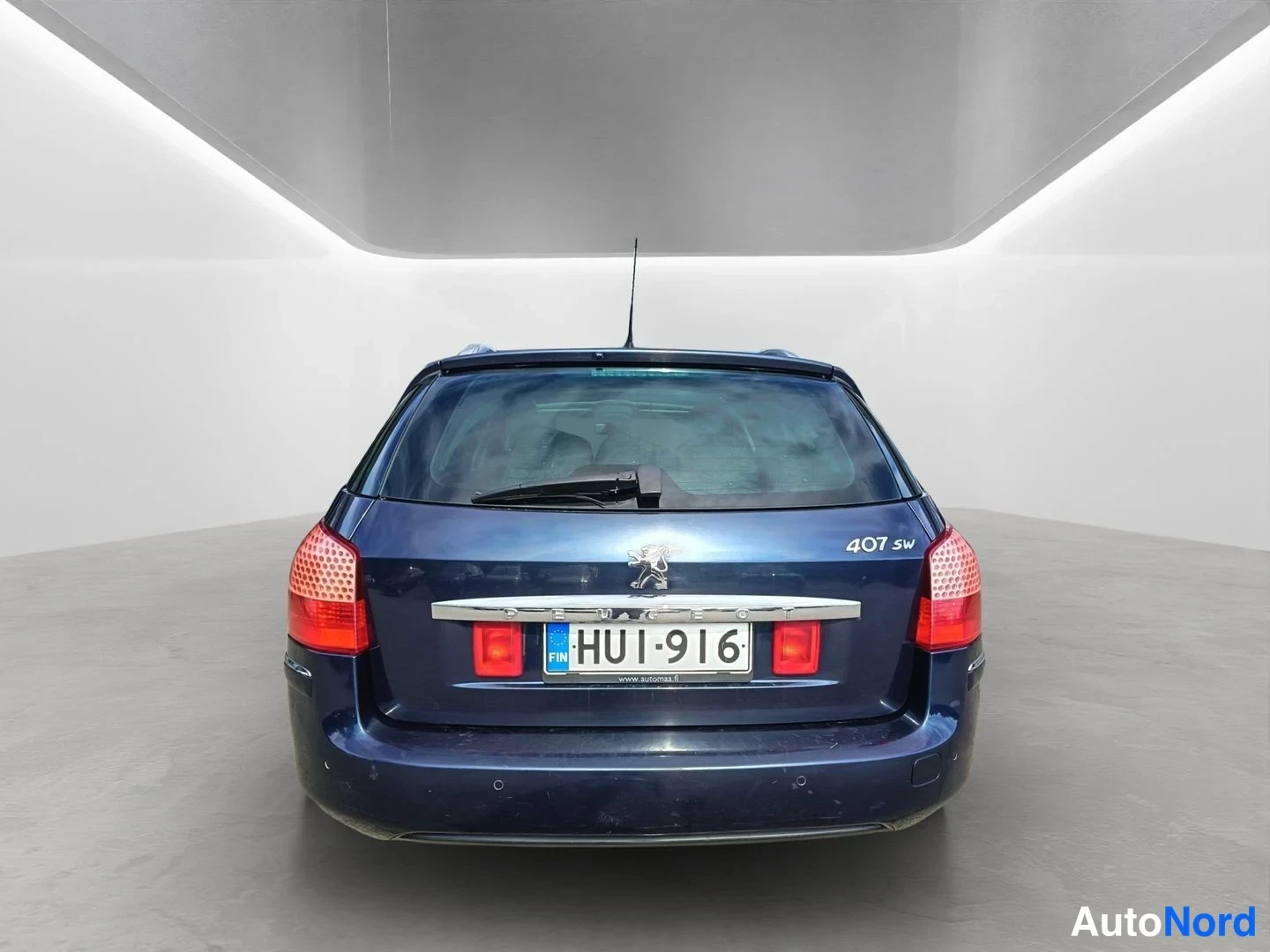 Takaa: Tummansinisen Peugeot 407 SW -farmarin takaosa suoraan takaa valokuvattuna. Takaluukussa kromilista PEUGEOT-tekstillä ja leijonatunnus sekä 407 SW -mallimerkki.
