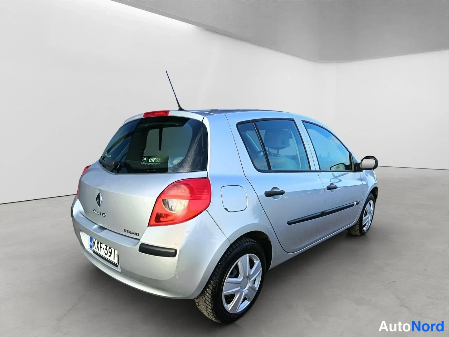 Takaviisto: Takaa vasemmalta otettu kuva hopeanharmaasta Renault Clistä. Auto on pysäköity valkoisessa tilassa.