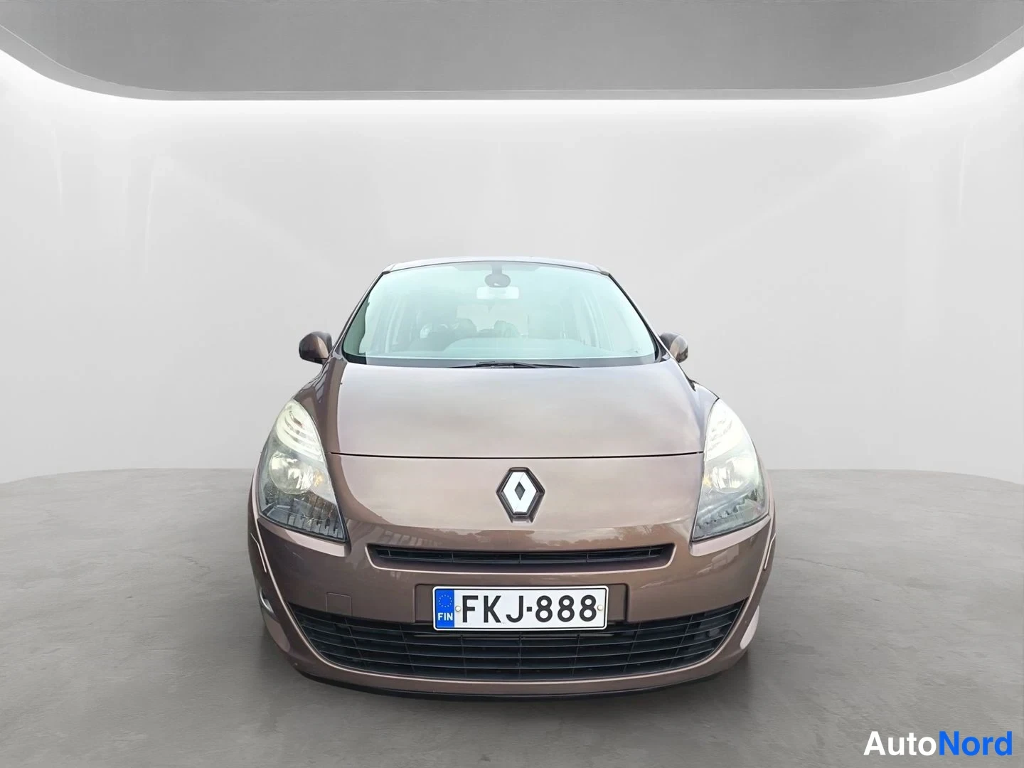 Edestä: Ruskea Renault Grand Scenic suoraan edestä päin kuvattuna. Näkyvissä Renault-merkki, ajovalot, etusäleikkö ja rekisterikilpi.