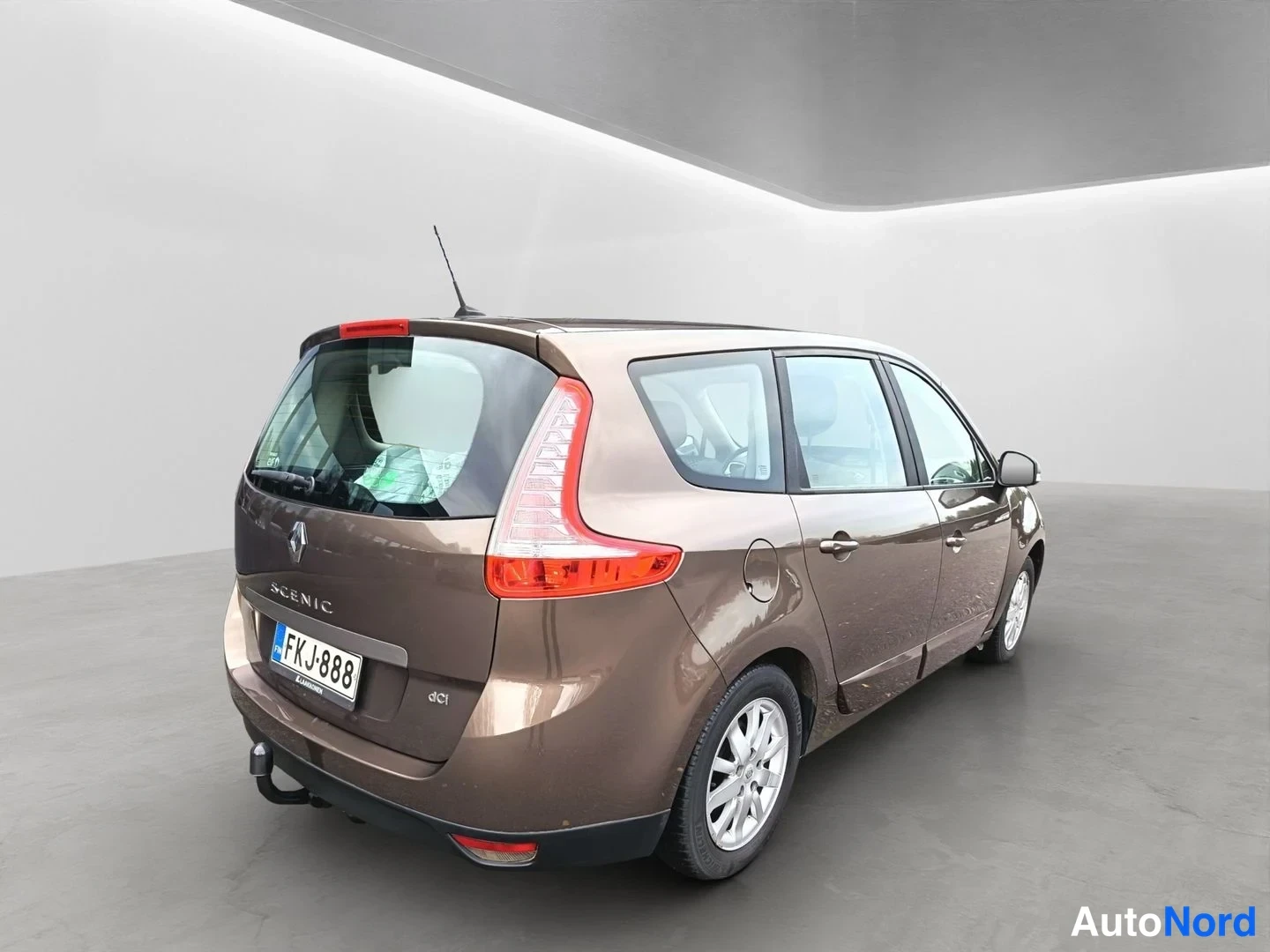 Takaviisto: Ruskea Renault Grand Scenic takaa oikealta kulmasta kuvattuna studiotiloissa; rekisterikilpi, dCi-merkintä ja vetokoukku näkyvissä.