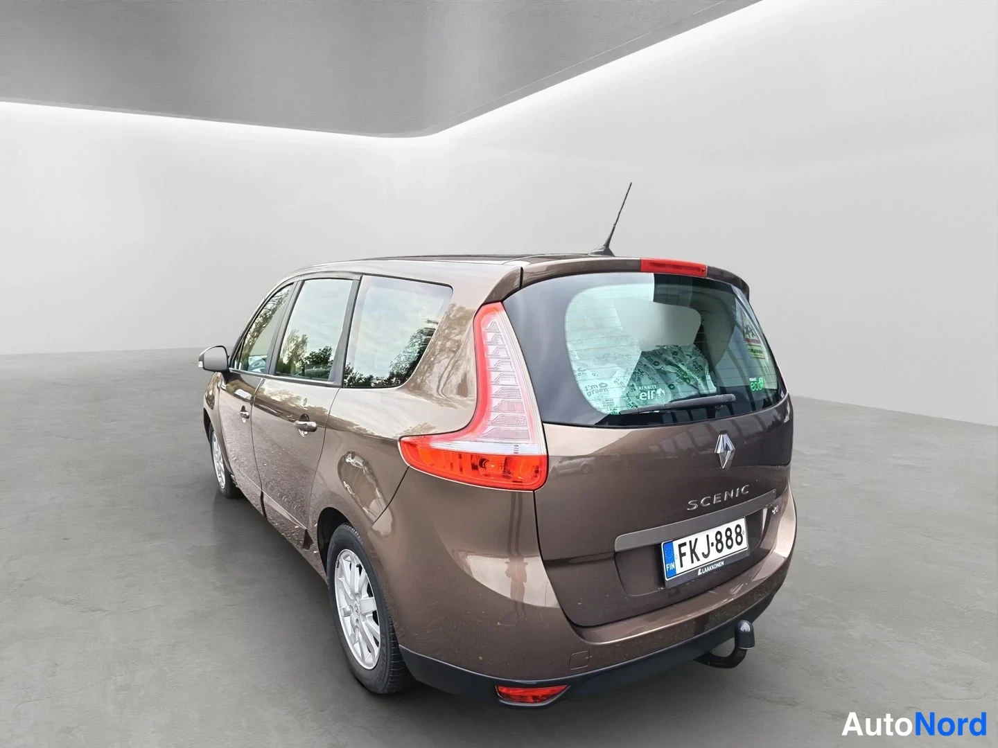 Takaviisto: Ruskea Renault Grand Scenic takaa vasemmalta kulmasta kuvattuna studiotiloissa; rekisterikilpi, dCi-merkintä ja vetokoukku näkyvissä.
