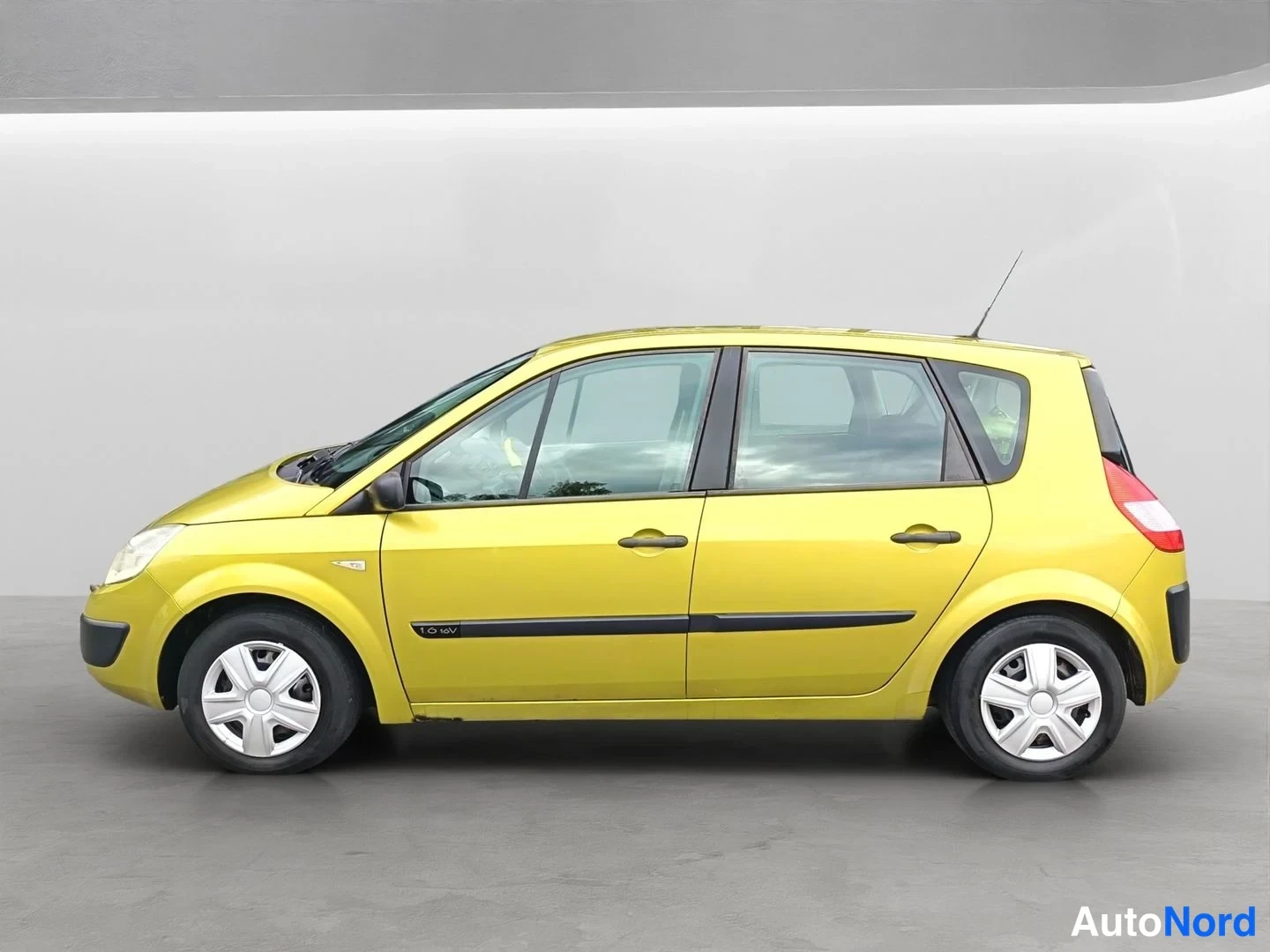 Etuviisto, nokka vasemmalle: Keltainen Renault Scenic -henkilöauto etuviistosta vasemmalta kuvattuna studioissa.