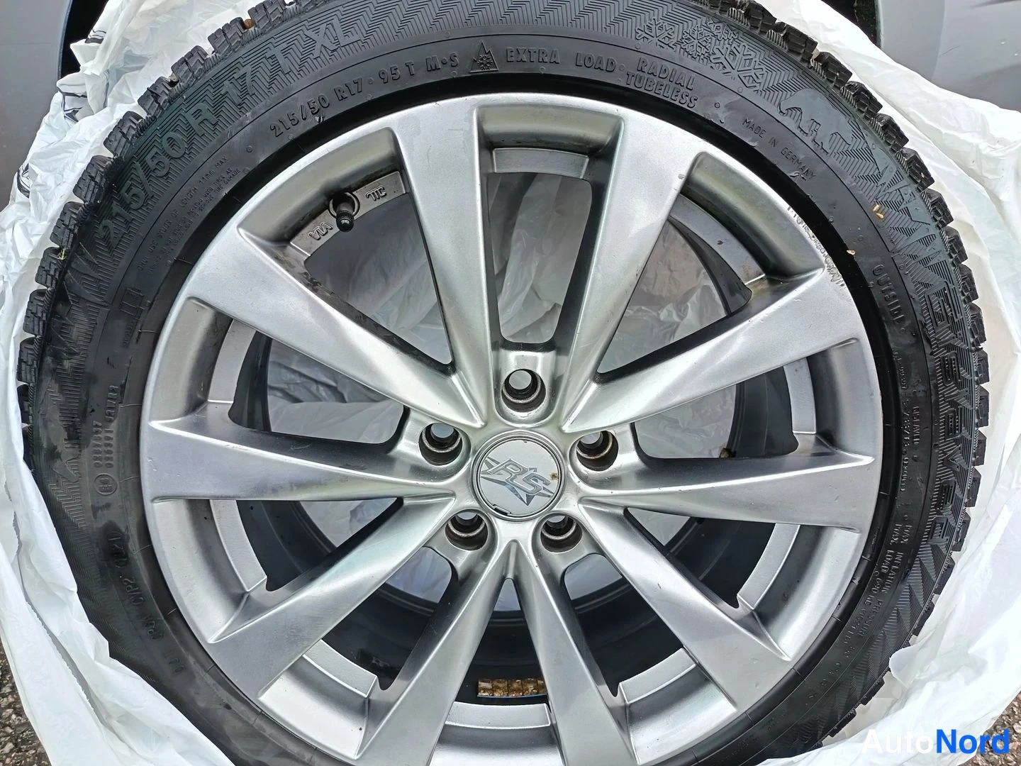 Muu: 235/50 R17 99T M+S -talvirenkaan keskellä hopeanvärinen alumiinivanne, peitetty valkoisella liinalla.