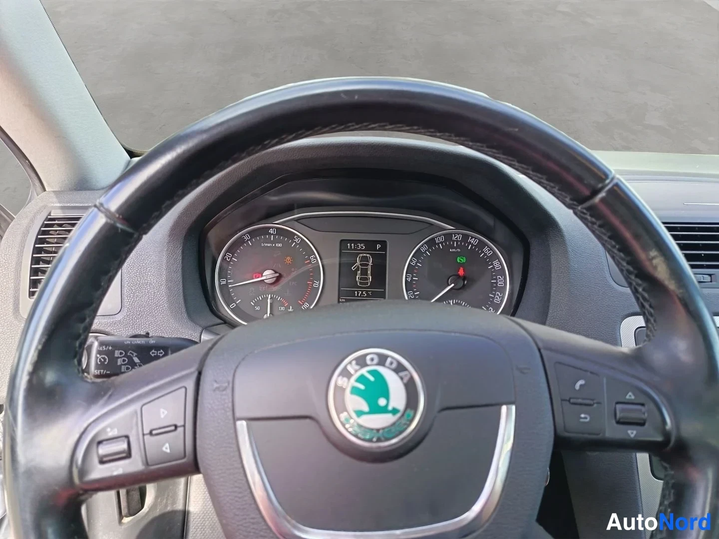Muu: Ohjaamon näkymä Skoda-ohjauspyörän läpi: mittaristo ja kosketusnäyttö näkyvät.