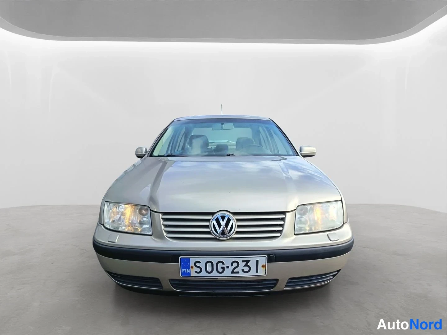 Edestä: Beige henkilöauto suoraan edestä kuvattuna, rekisterikilpi, valoisassa studiossa.