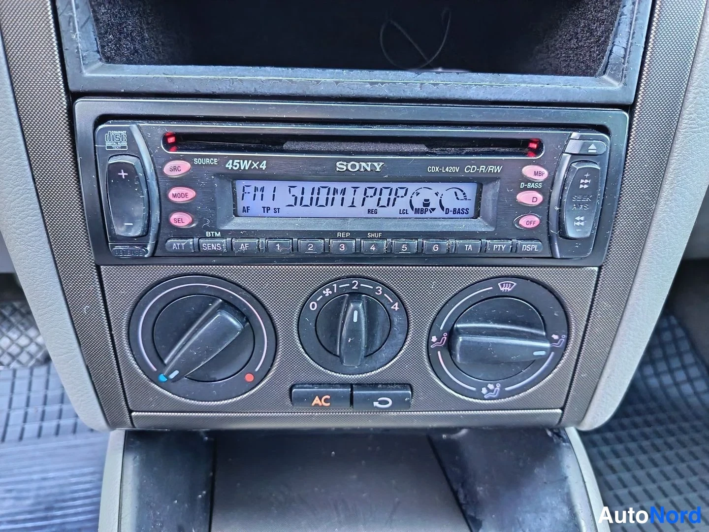 Ohjaamo: Close-up of the center console featuring a Sony CD player/radio unit above three rotary climate control dials. An illuminated orange AC button is visible below