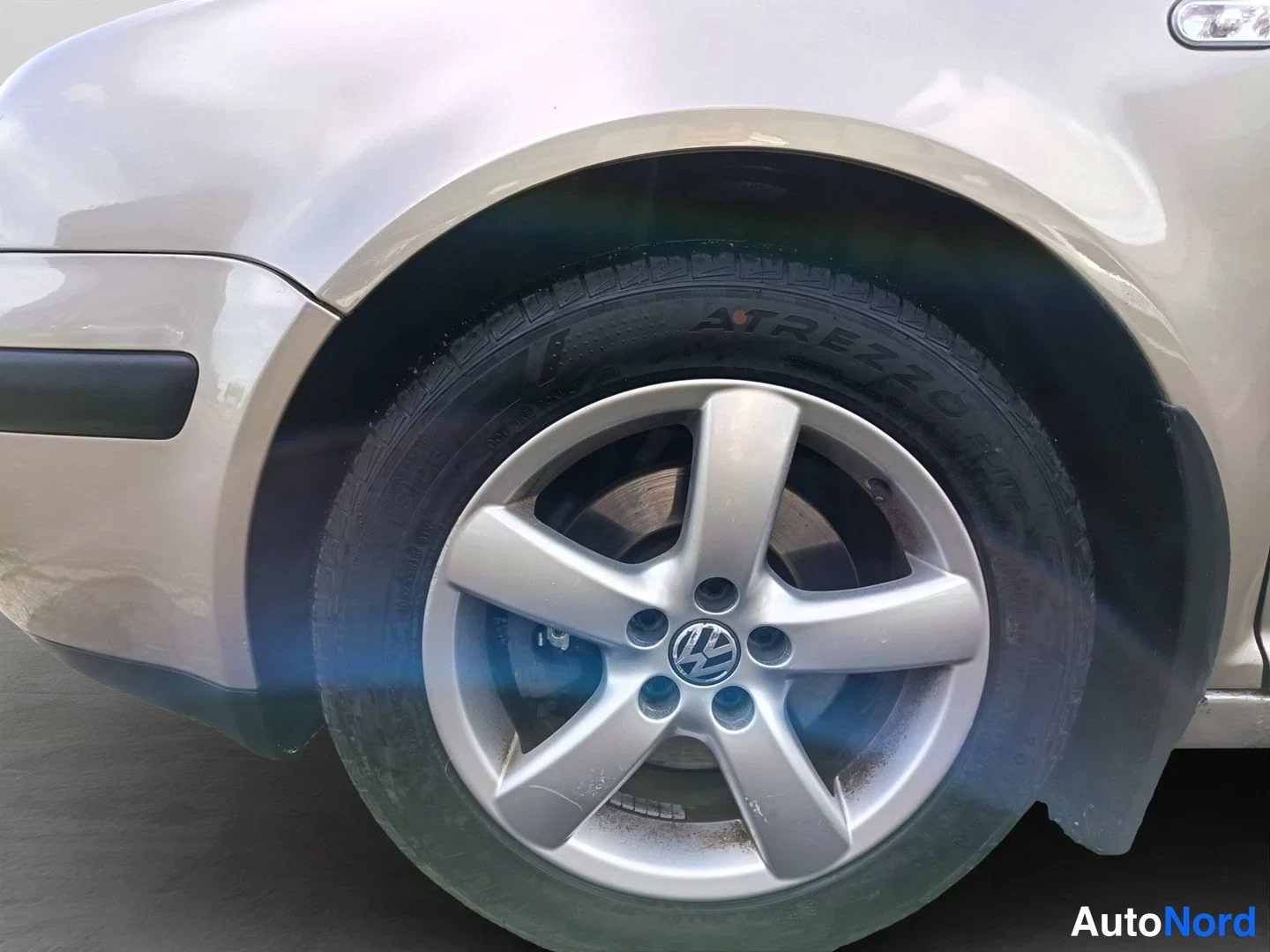 Yksityiskohta: Kuvan etupään kulma jossa on valkoinen kevytmetallivanteet ja Volkswagen-logo. Osittainen näkyvyys keulasta ja ovien reunasta.