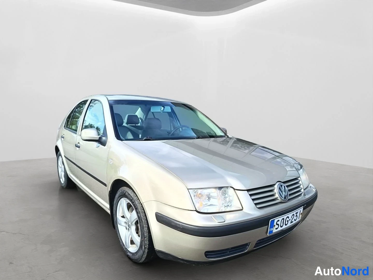 Etuviisto, nokka oikealle: Beige henkilöauto kuvattuna etuoikealta kolmannesta, rekisterikilpi, harmaassa studiossa.