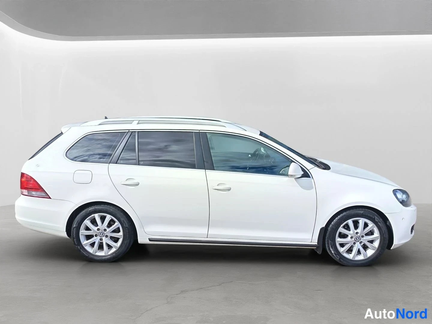 Sivulta: Valkoinen Volkswagen Station Wagon kyljessä, jossa on selkeästi näkyvissä sivupintaa, leveät alumiini-renkaat ja katto-kiskot.