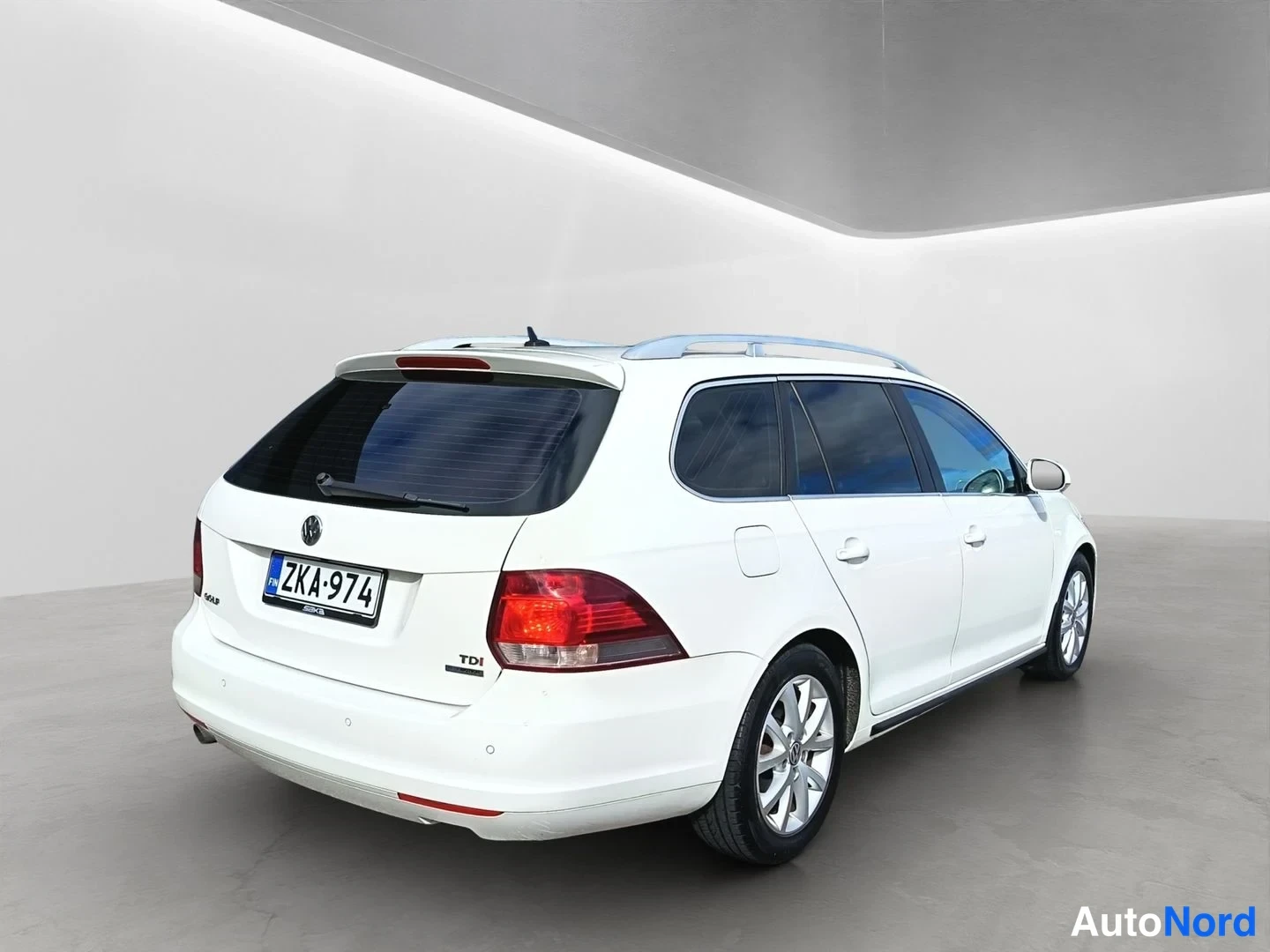 Takaviisto: A white Volkswagen Golf station wagon photographed from a rear three-quarter angle, showing the rear tail lights and the right flank of the car. Silver roof rai