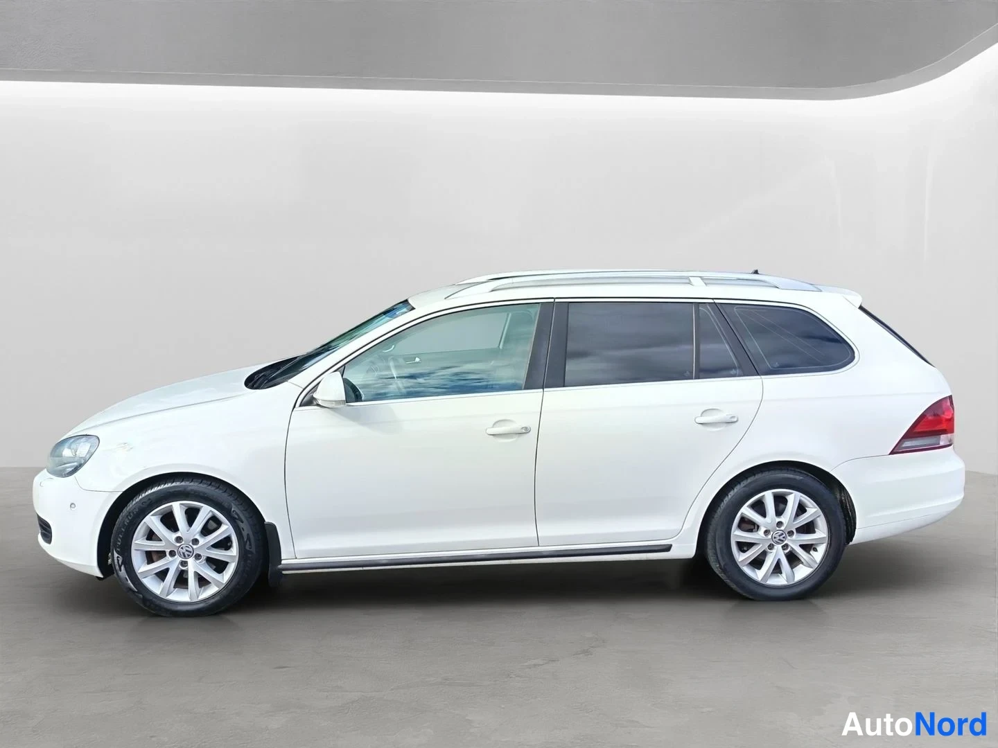 Sivulta: Full side profile of the white station wagon against a light background. Silver multi-spoke alloy wheels are on both front and rear axles. Roof rails are mounte