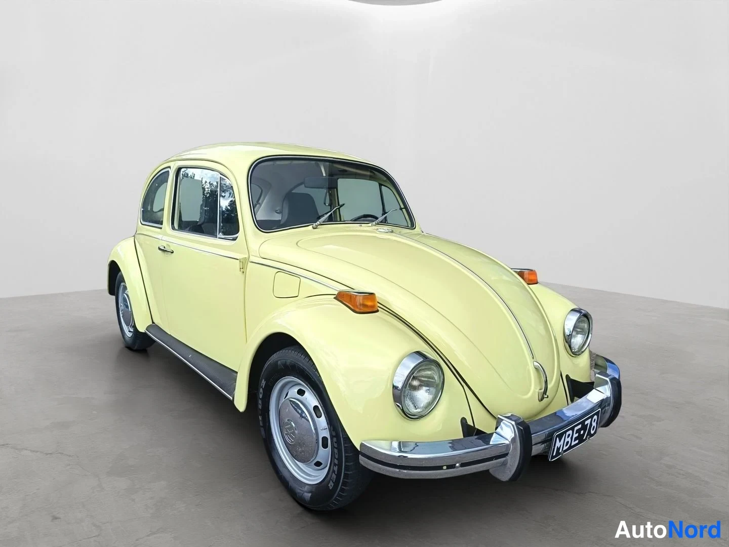 Etuviisto, nokka oikealle: Keltainen Volkswagen Kupla etuviistöstä oikealle suunnattuna, rekisteritunnus näkyvissä.