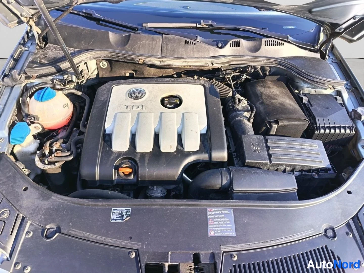 Muu: Moottoritila avattuna: Volkswagen TDI-merkitty moottorin suojakansi, jäähdytysainesäiliö ja ilmansuodatinlaatikko näkyvät.
