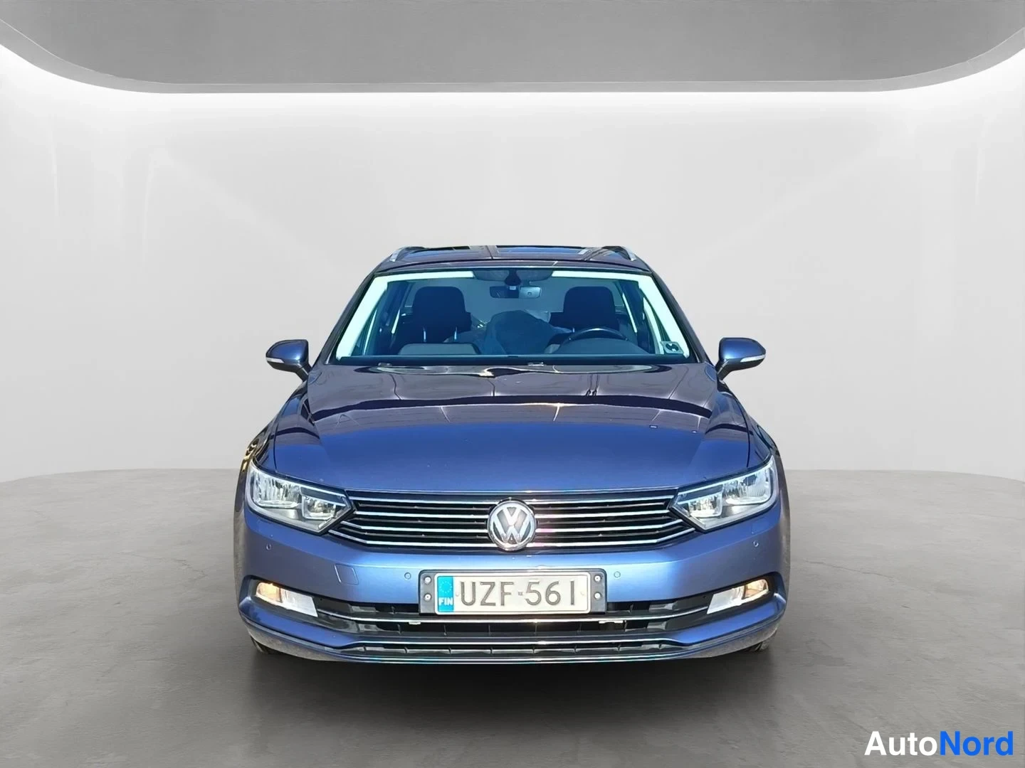 Edestä: Sinisen Volkswagen Passat Variantin suora eduskva, josta näkyvät etusäleikkö, VW-merkki, ajovalot ja rekisteritunnus.