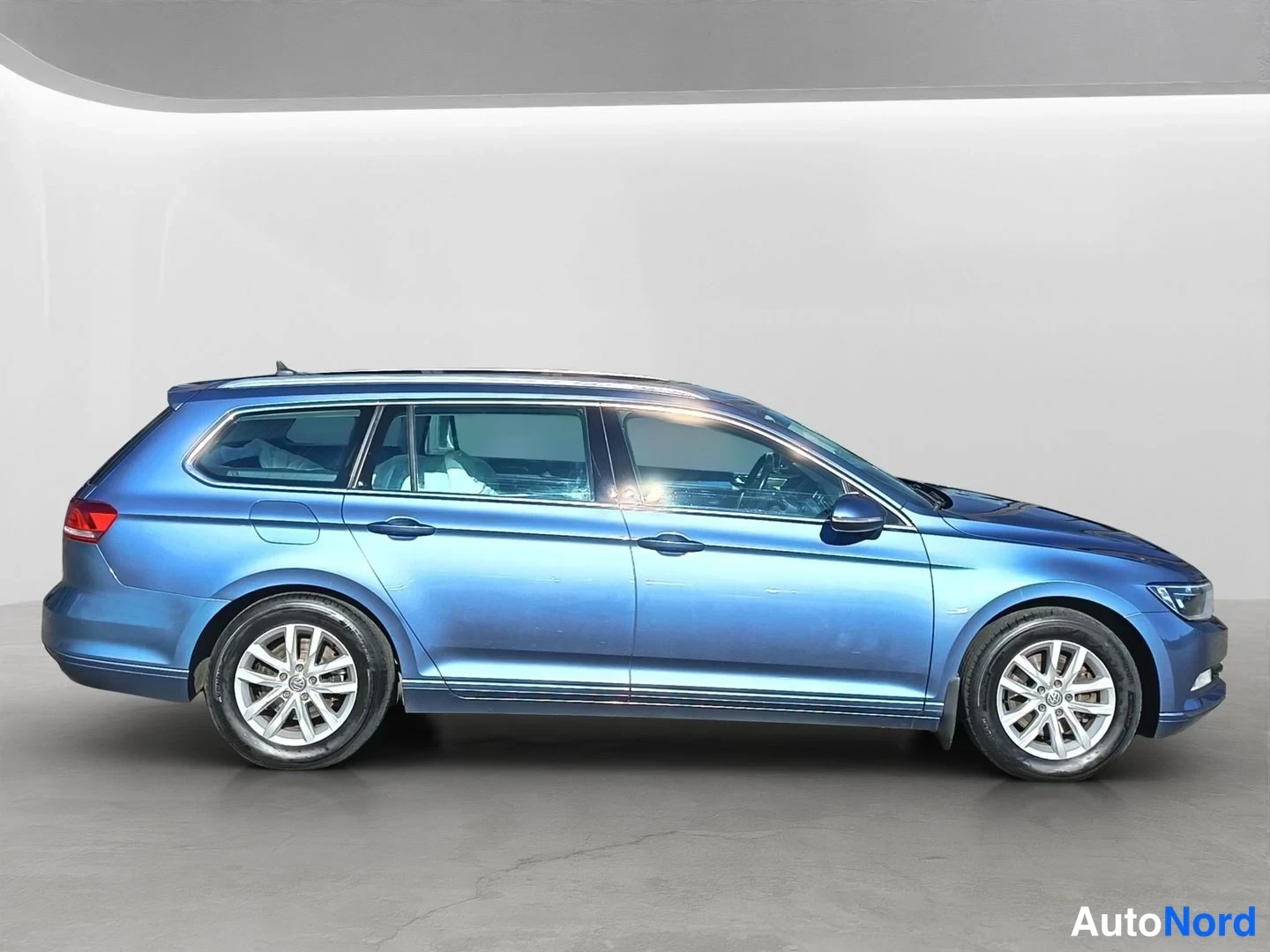 Sivulta: Sininen Volkswagen Passat Variant suoraan sivulta nähtynä, kylki ja molemmat pyörät täysin näkyvissä, kattoaallonpää ja taustavalon reuna erottuvat.
