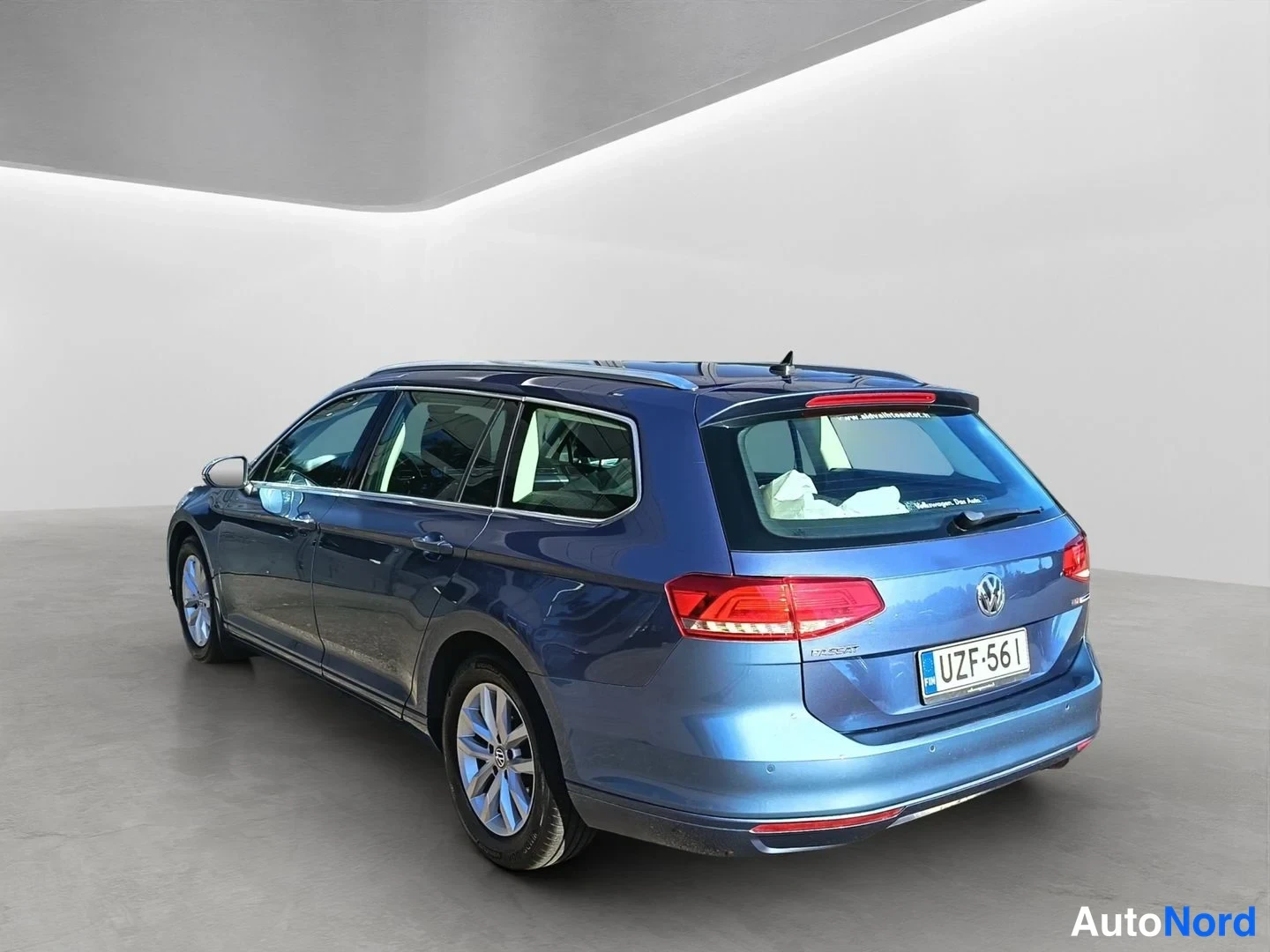 Takaviisto: Blue Volkswagen Passat Variant photographed from the left rear three-quarter angle showing the tailgate, left flank and wheels against a white studio background