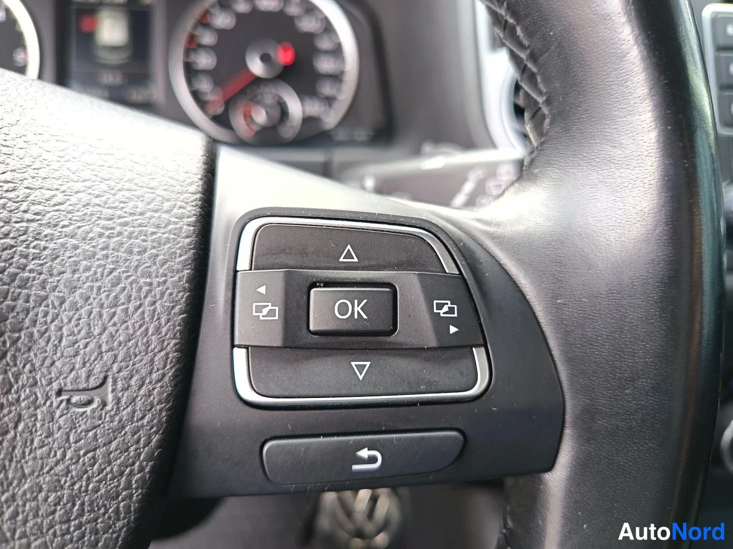 Yksityiskohta: Close-up of the steering wheel with multifunction buttons including OK, up/down arrows, and return symbol.