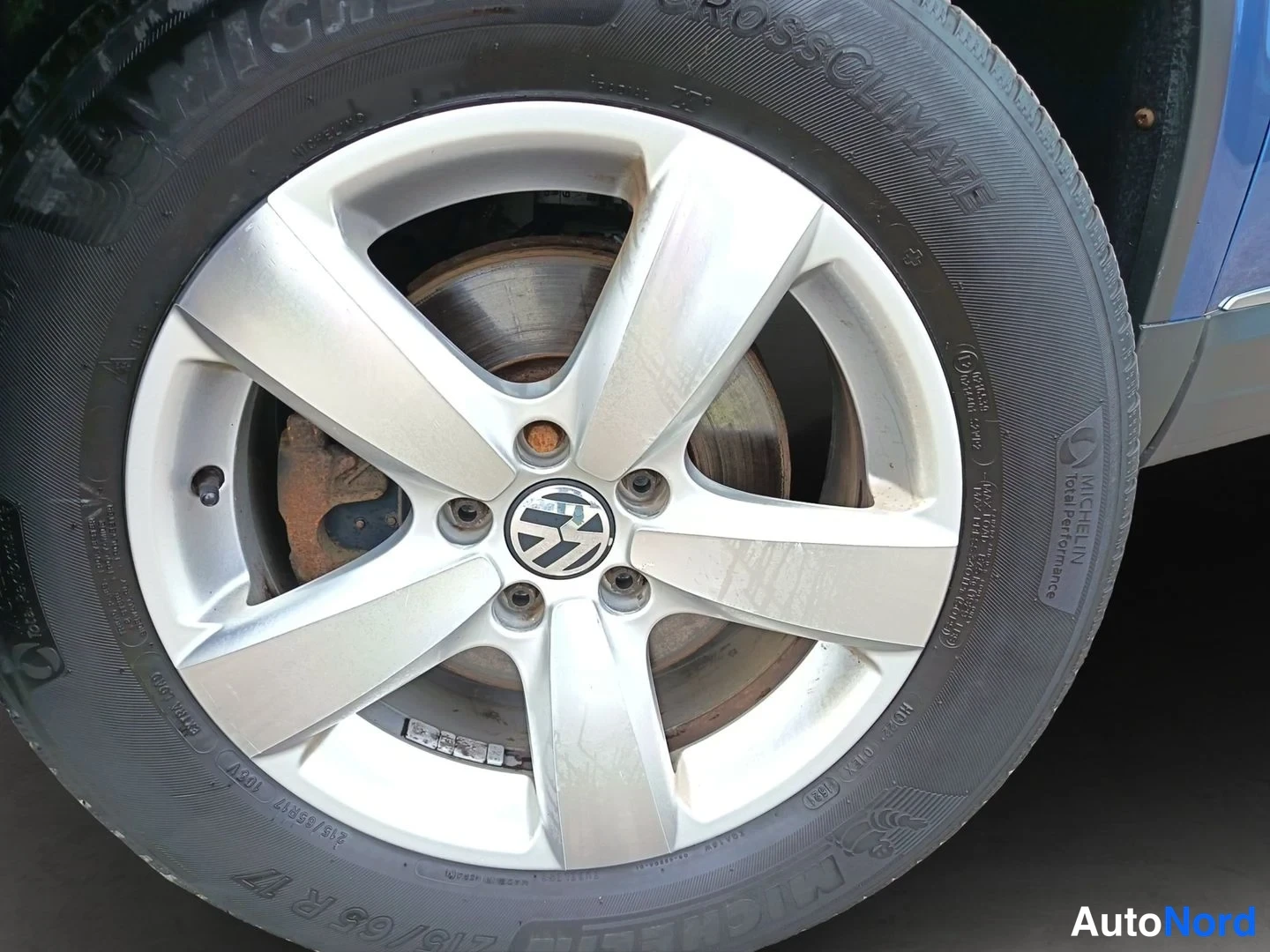 Muu: Volkswagenin hopeinen viisipuolainen alumiinivanne, Michelin CrossClimate -rengas ja jarrulevy pölyisellä ja ruosteisella napakalla.