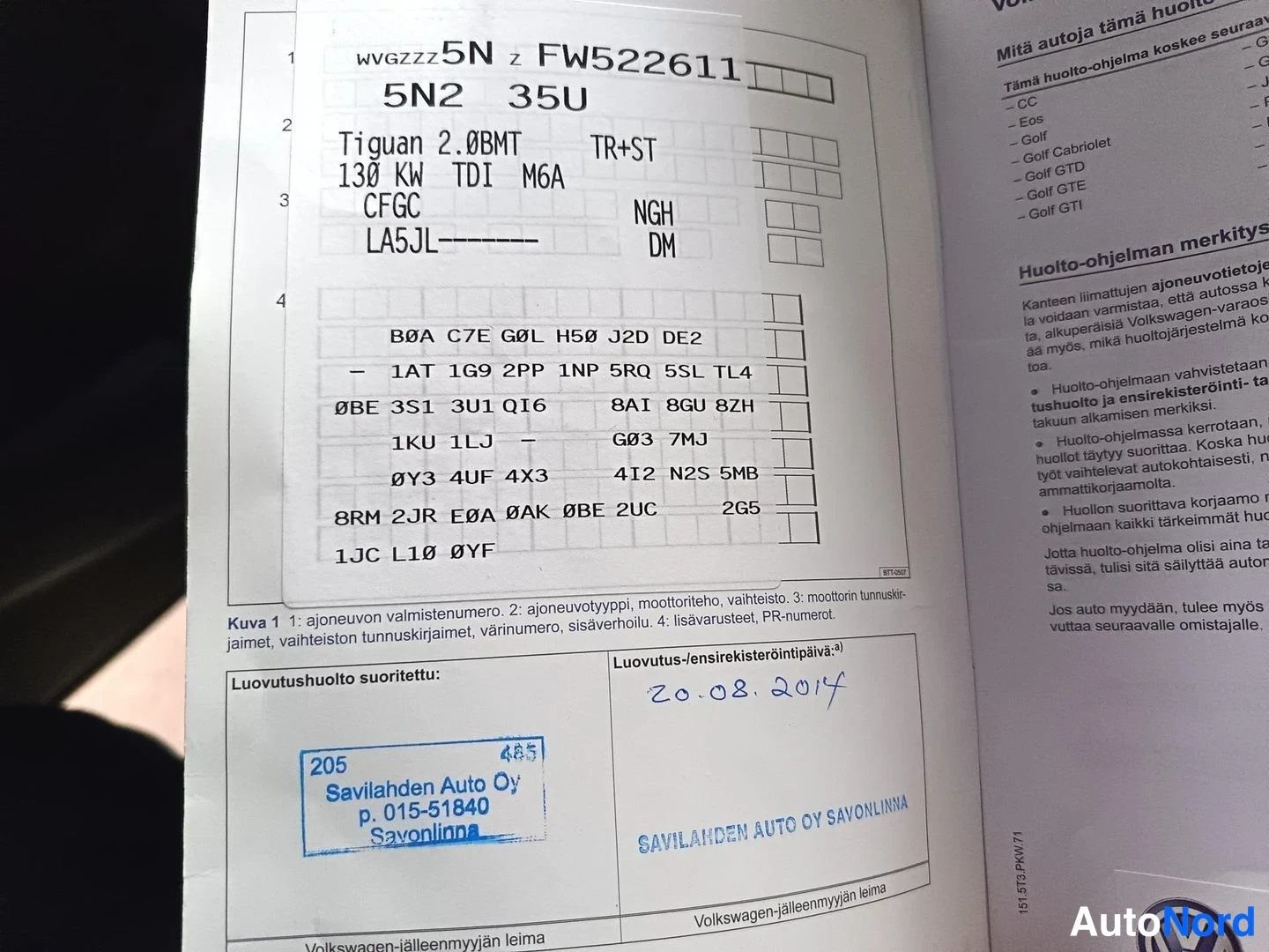 Yksityiskohta: Huoltokirjan sivu, jossa ajoneuvon tunnisteet: Volkswagen Tiguan 2.0 TDI, VIN FW522611, ja leima Savilahden Auto Oy Savonlinnasta, luovutushuolto 20.8.2014.