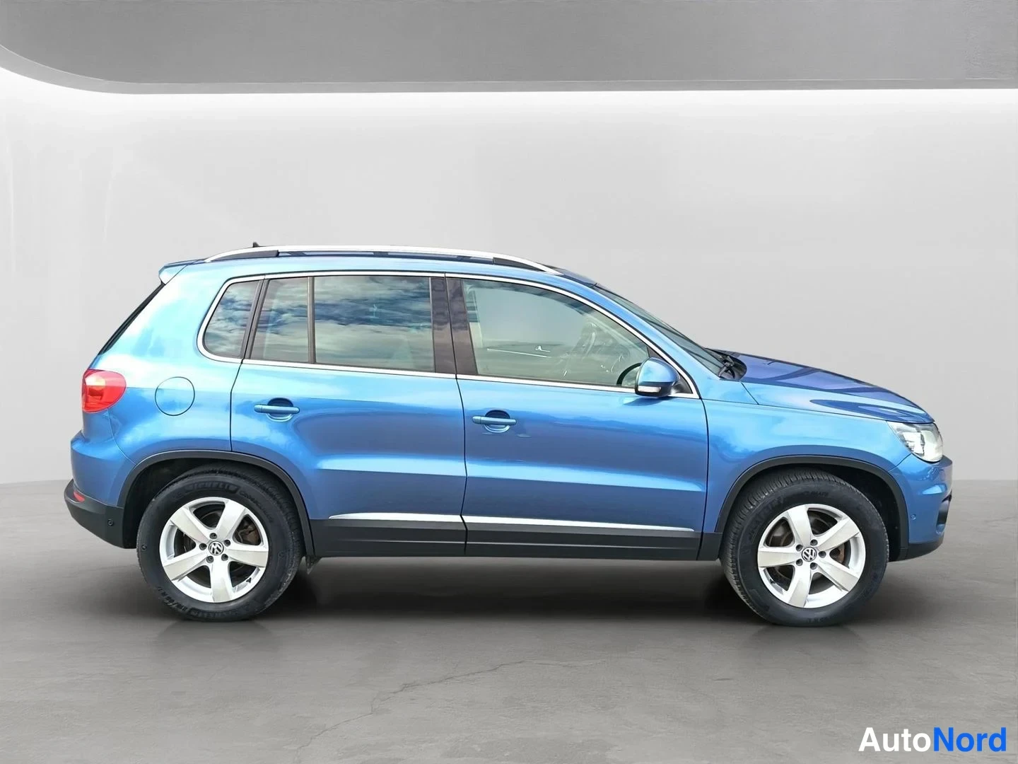 Sivulta: Sininen Volkswagen Tiguan sivulta oikealta, kattokaiteet ja hopeat levyt.