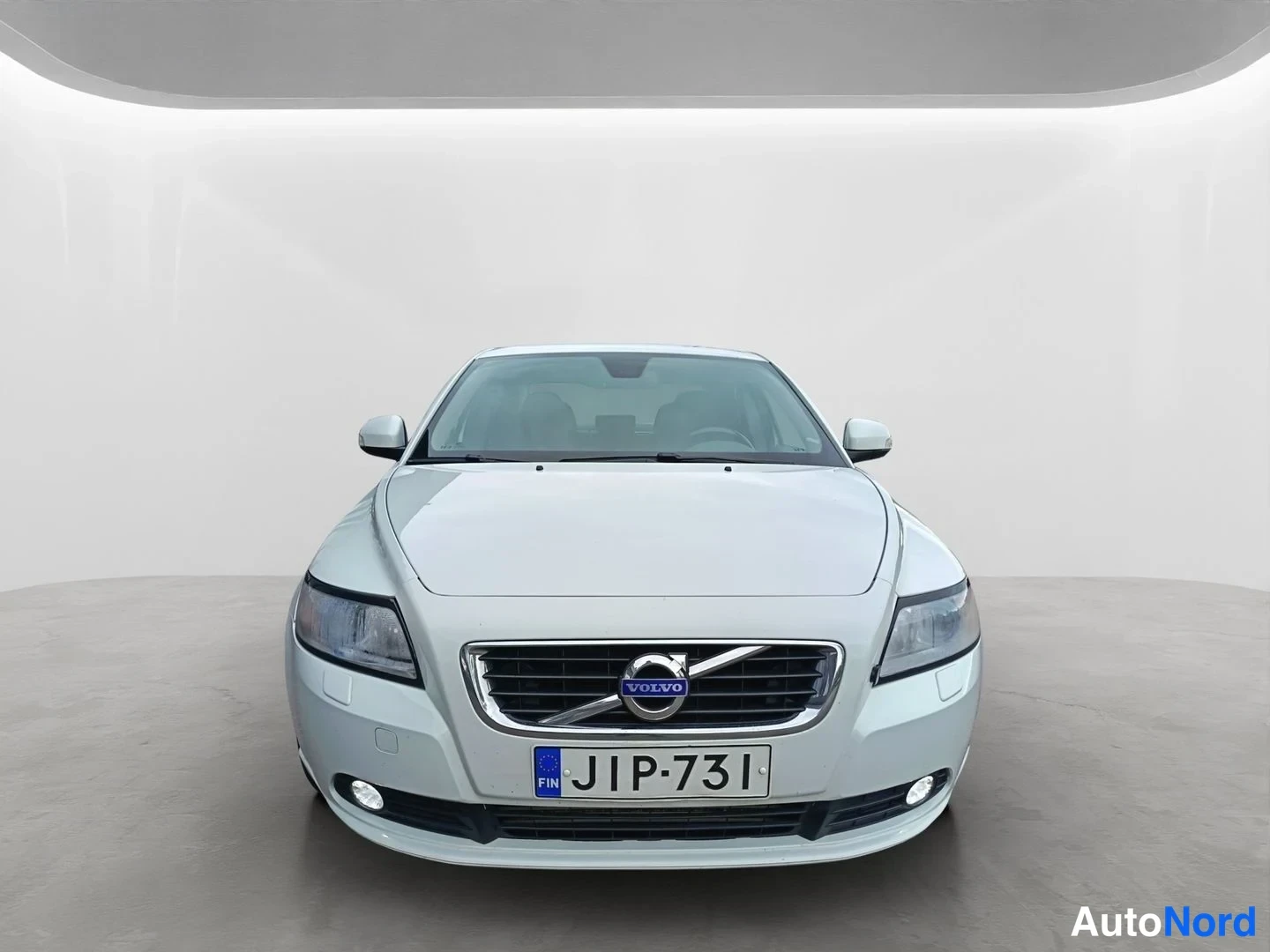Edestä: Direct front view of a white Volvo sedan showing the grille, headlights and license plate.