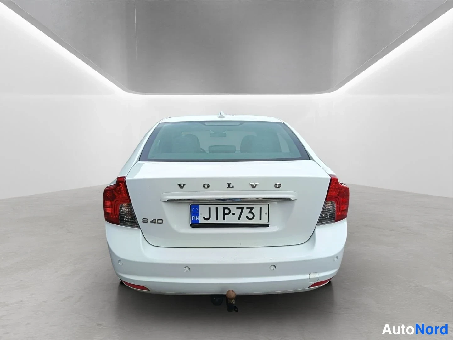 Takaa: Suora takakuva valkoisesta Volvo S40 -sedanista, jossa näkyy rekisterinumero ja perävaunun kytkin.