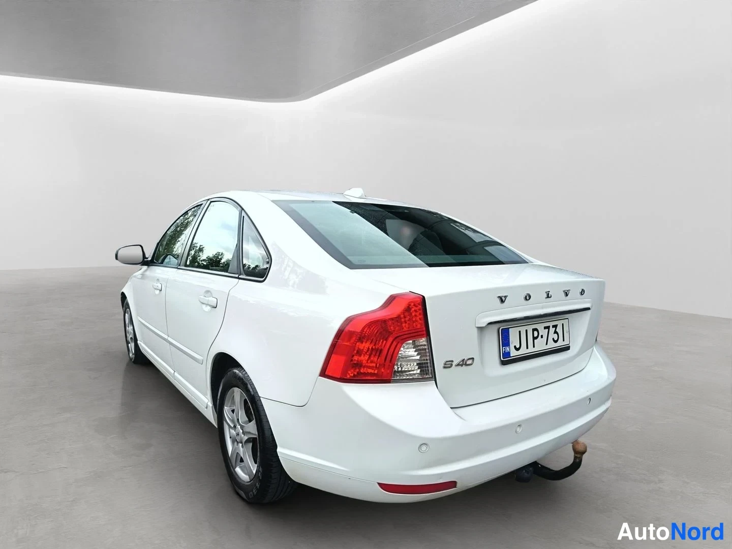 Takaviisto: Valkoinen Volvo sedan kuvattuna takaa kolmanteen kulmaan oikealla, perävaunun kytkin ja vanteet näkyvät.