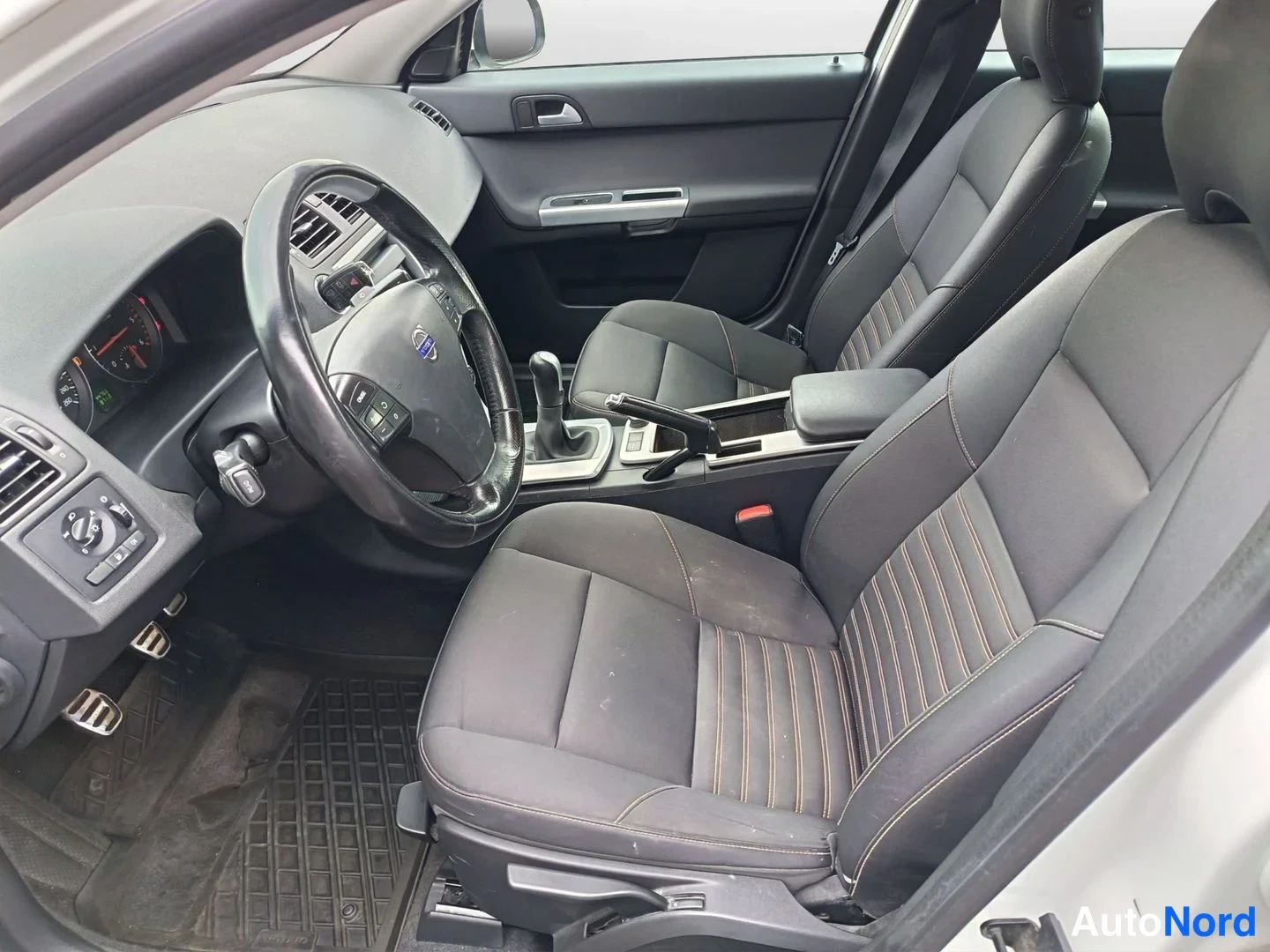 Ohjaamo: Interior view from the passenger side, showing the driver's seat and steering wheel on the left, automatic gear selector, centre armrest, and part of the front