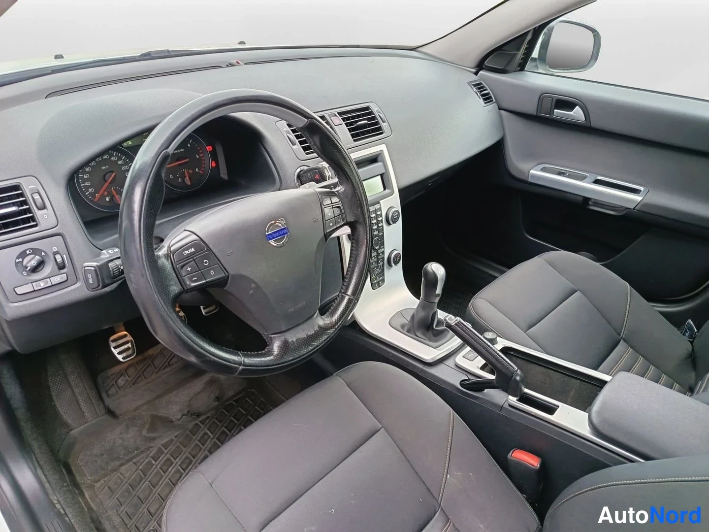 Etuistuimet: Front cabin view taken from inside near the driver's side A-pillar looking right. Steering wheel with mounted audio controls is central, dashboard and instrumen