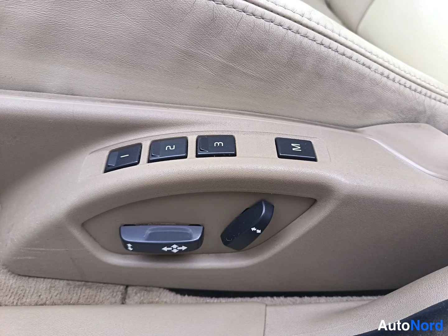 Yksityiskohta: Driver's door armrest shows memory seat buttons labeled M, 1, 2, and 3 next to electric seat shape controls on beige material.