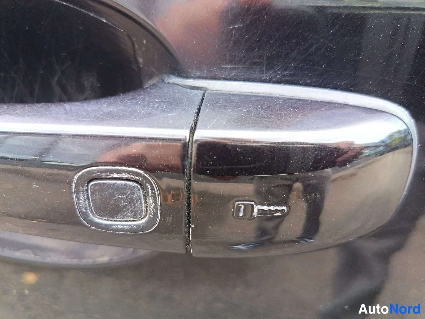 Yksityiskohta: Chrome door handle close-up with a keyhole and an integrated button for keyless entry visible on the exterior trim.