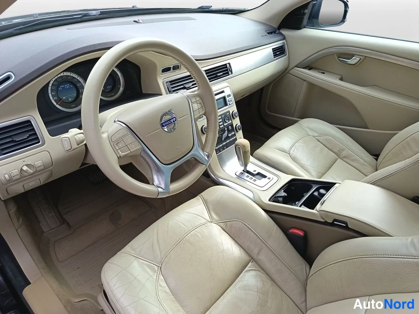 Etuistuimet: High-angle view of the interior cabin focused on the steering wheel, instrument cluster, and center console. The automatic gear selector has a light-colored woo