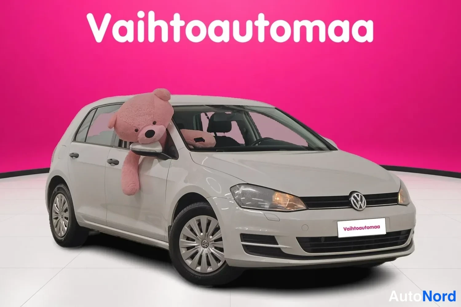 Etuviisto, nokka oikealle: Valkoinen Volkswagen-kirjoitettuna etuosa ja oikea sivu kolmen neljänneskuvan kulmasta, jossa vaaleanpunainen karhu istuu ohjaamossa näkyvänä.