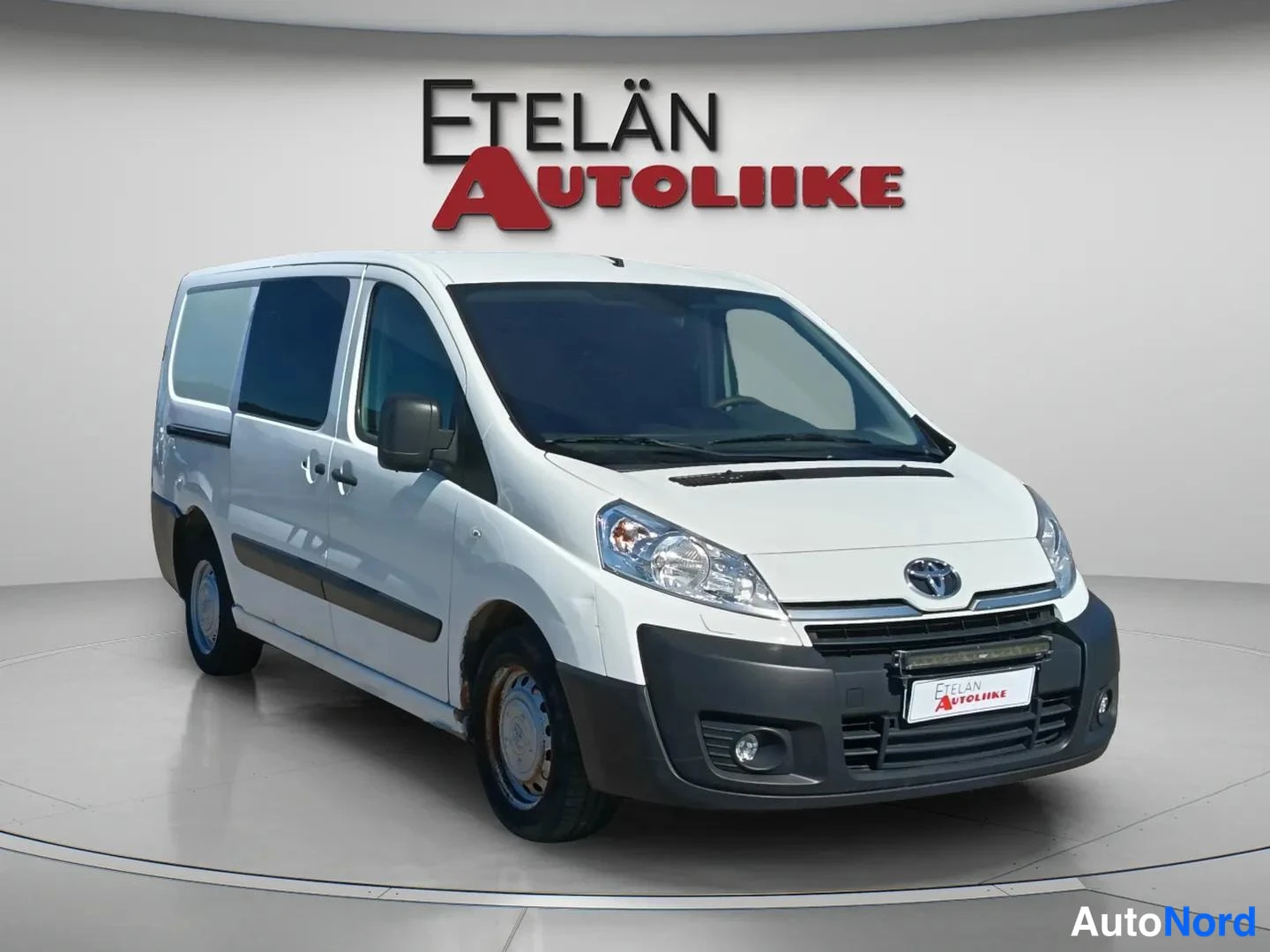 Etuviisto, nokka oikealle: Valkoinen Toyota Proace -pakettiauto etukolmanneskuvassa, keula kuvan oikeassa laidassa; tummennetut sivuikkunat ja etusäleikön edessä oleva vaakasuora v