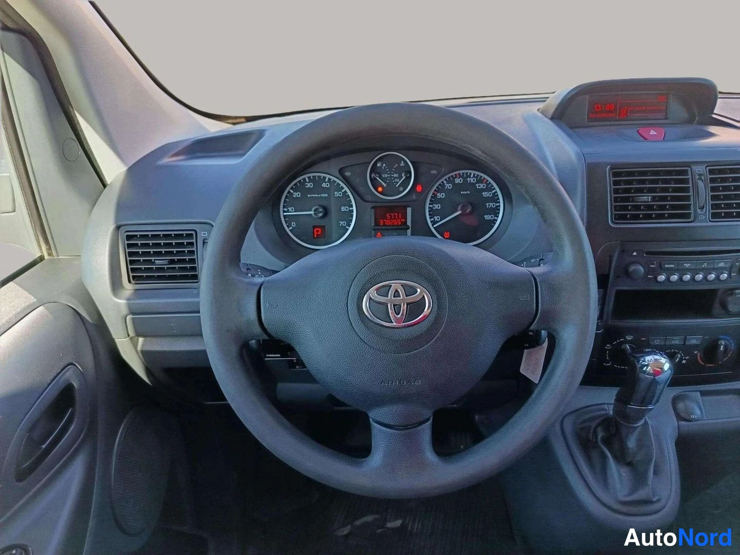 Yksityiskohta: Ohjaamon näkymä: Toyota-merkkinen ohjauspyörä, mittaristo, radiopaneeli ja manuaalivaihteen keila; matkamittarinäyttö lukee 378265 km.