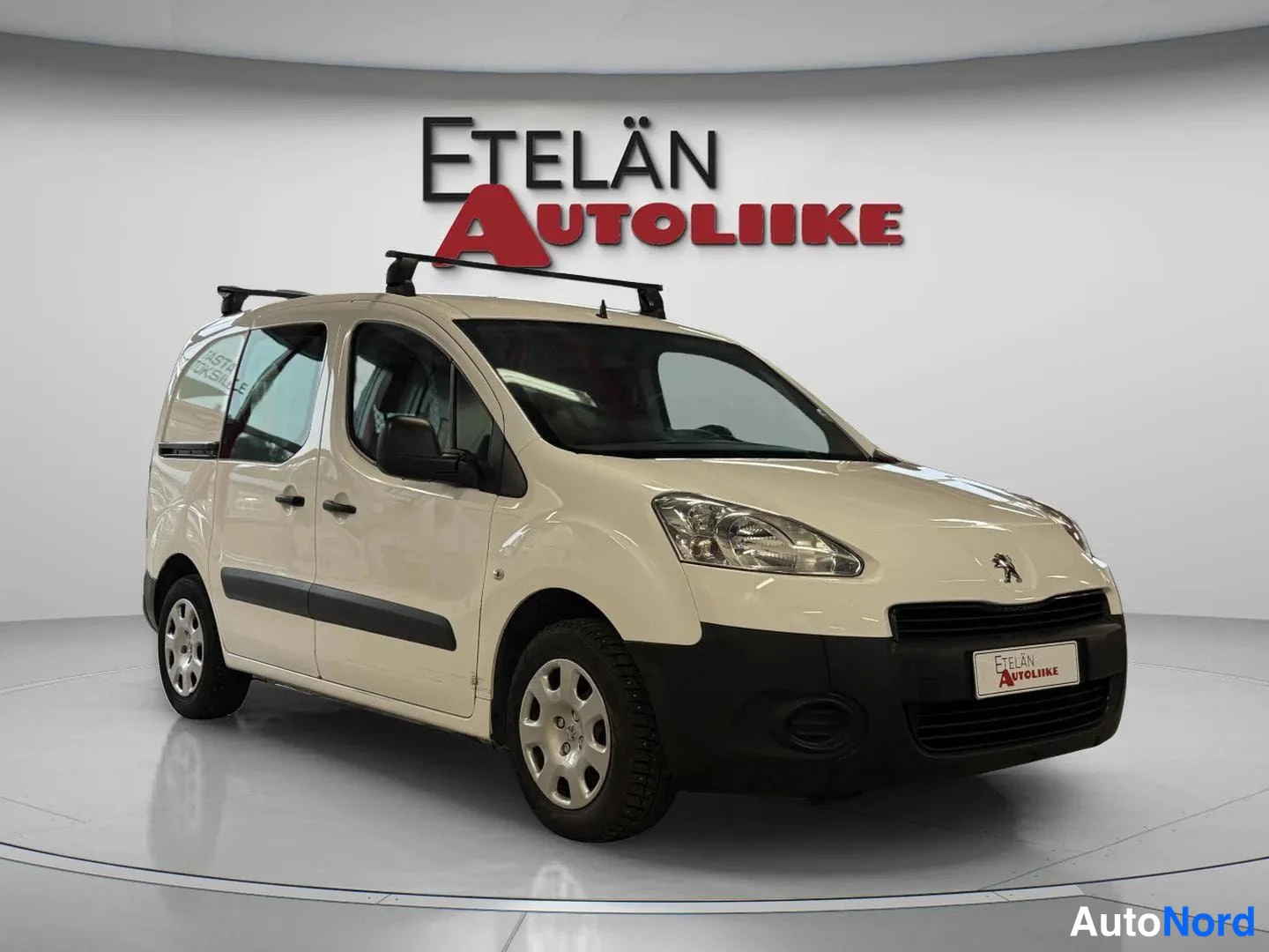 Etuviisto, nokka oikealle: Valkoinen Peugeot Partner etuviistosta, nokka oikealla; kattoteline katolla.